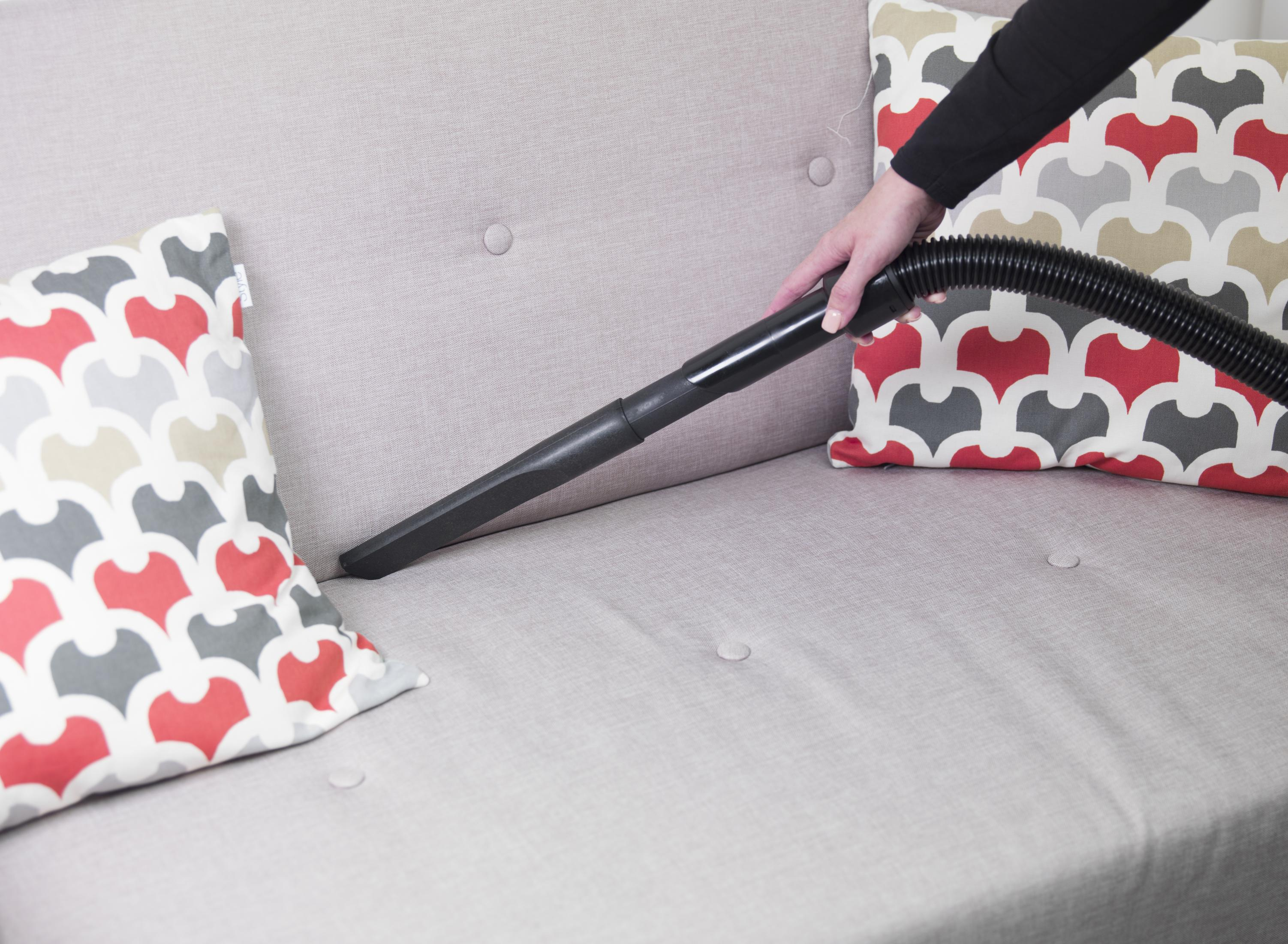Osoba odkurzająca sofę wąską dyszą, dwa poduszki z boku.