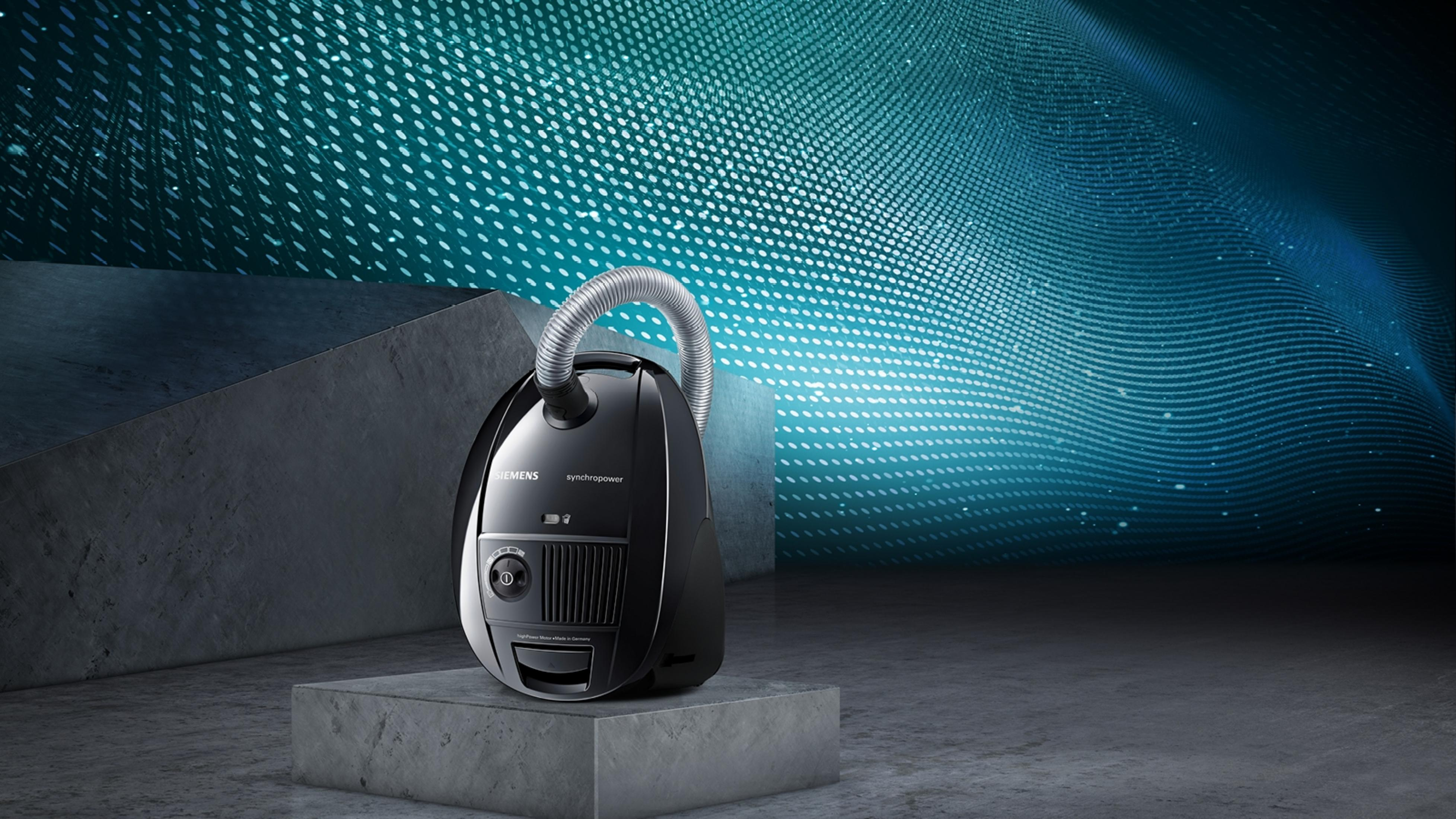 Czarny odkurzacz Siemens na betonowym cokole na tle turkusowego, wzorzystego tła.