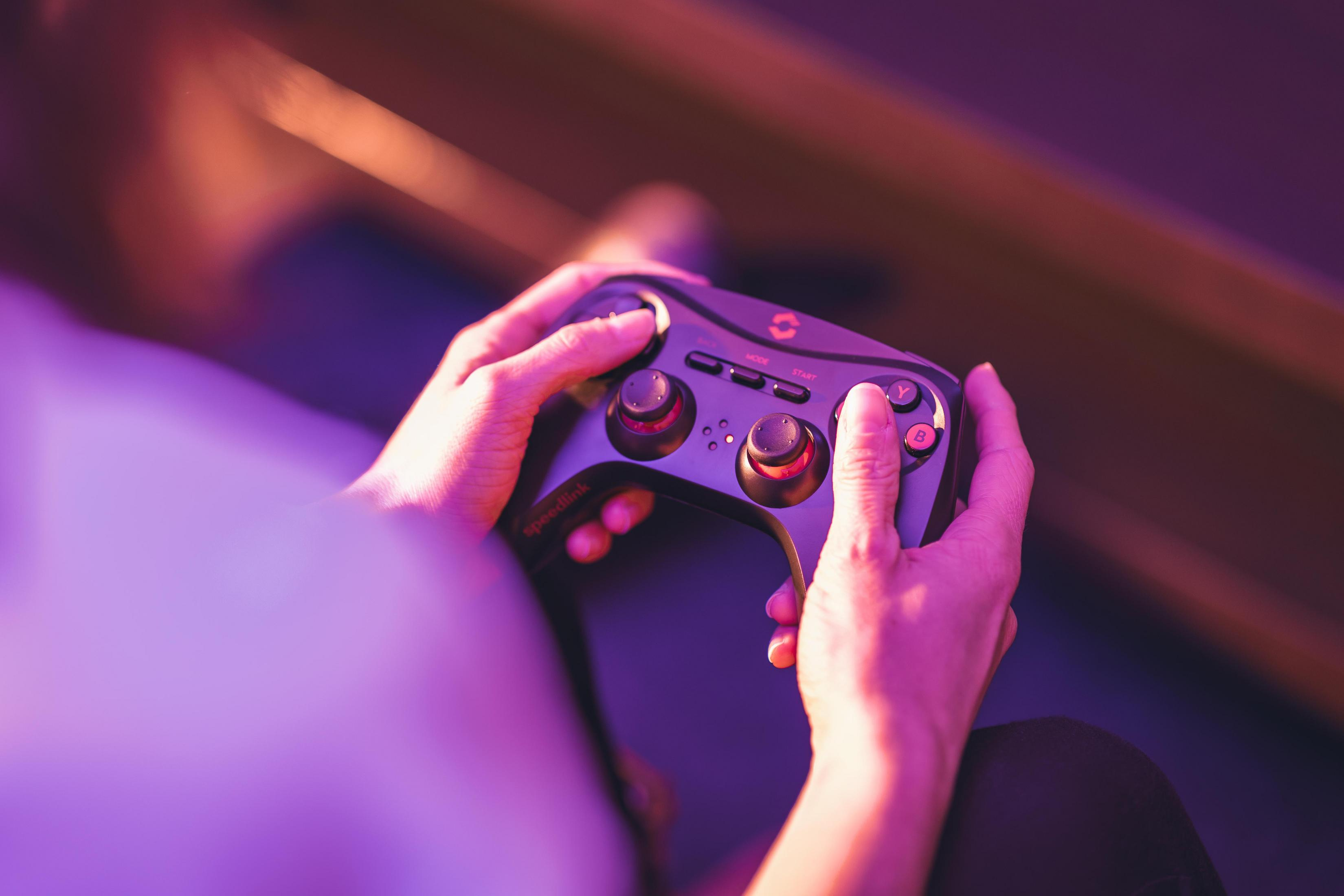 Dłonie trzymające czarny kontroler do gier. Kontroler ma czerwone przyciski. Tło jest rozmyte.