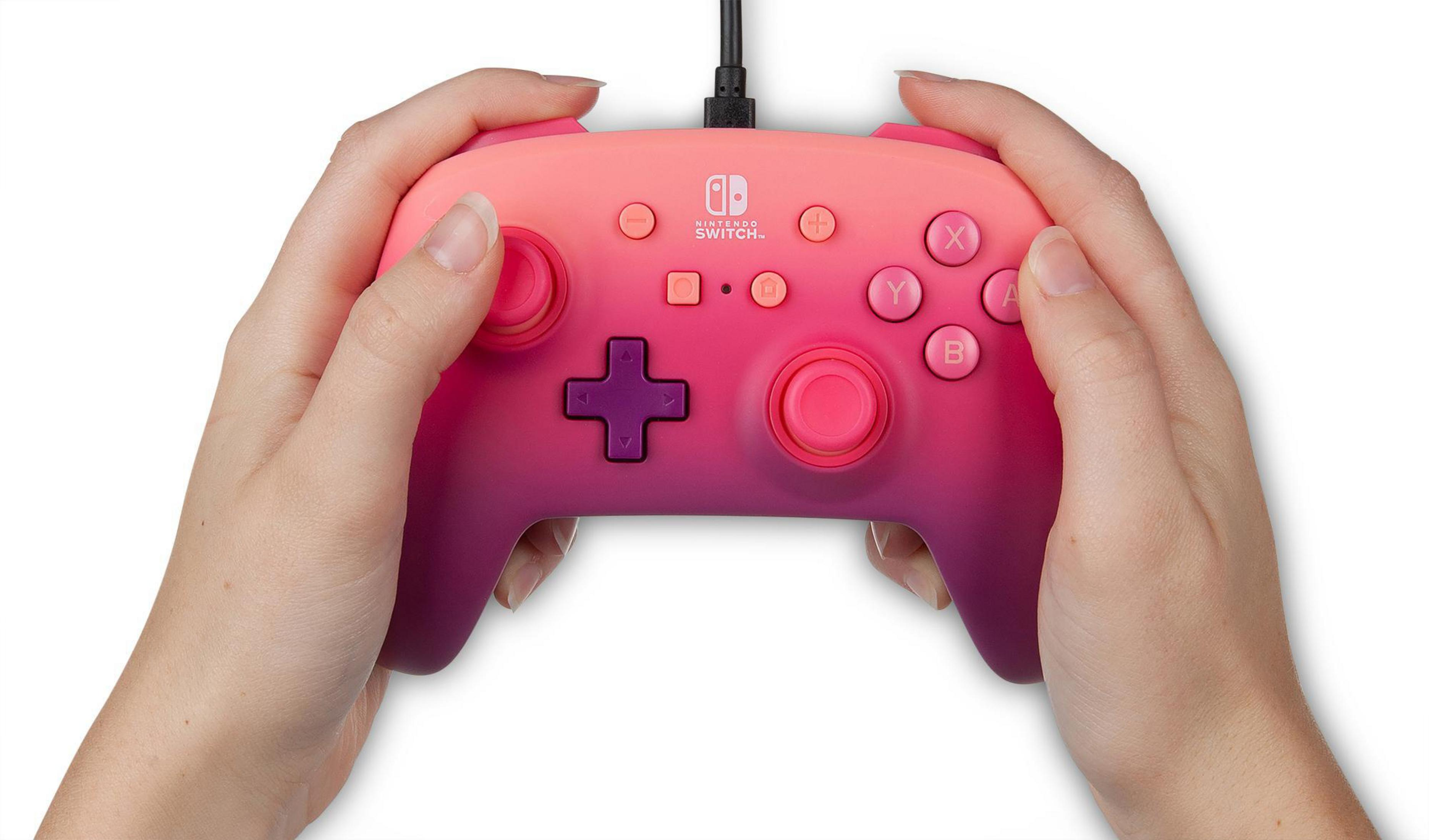 Dłonie trzymające różowo-fioletowy kontroler Nintendo Switch na białym tle.