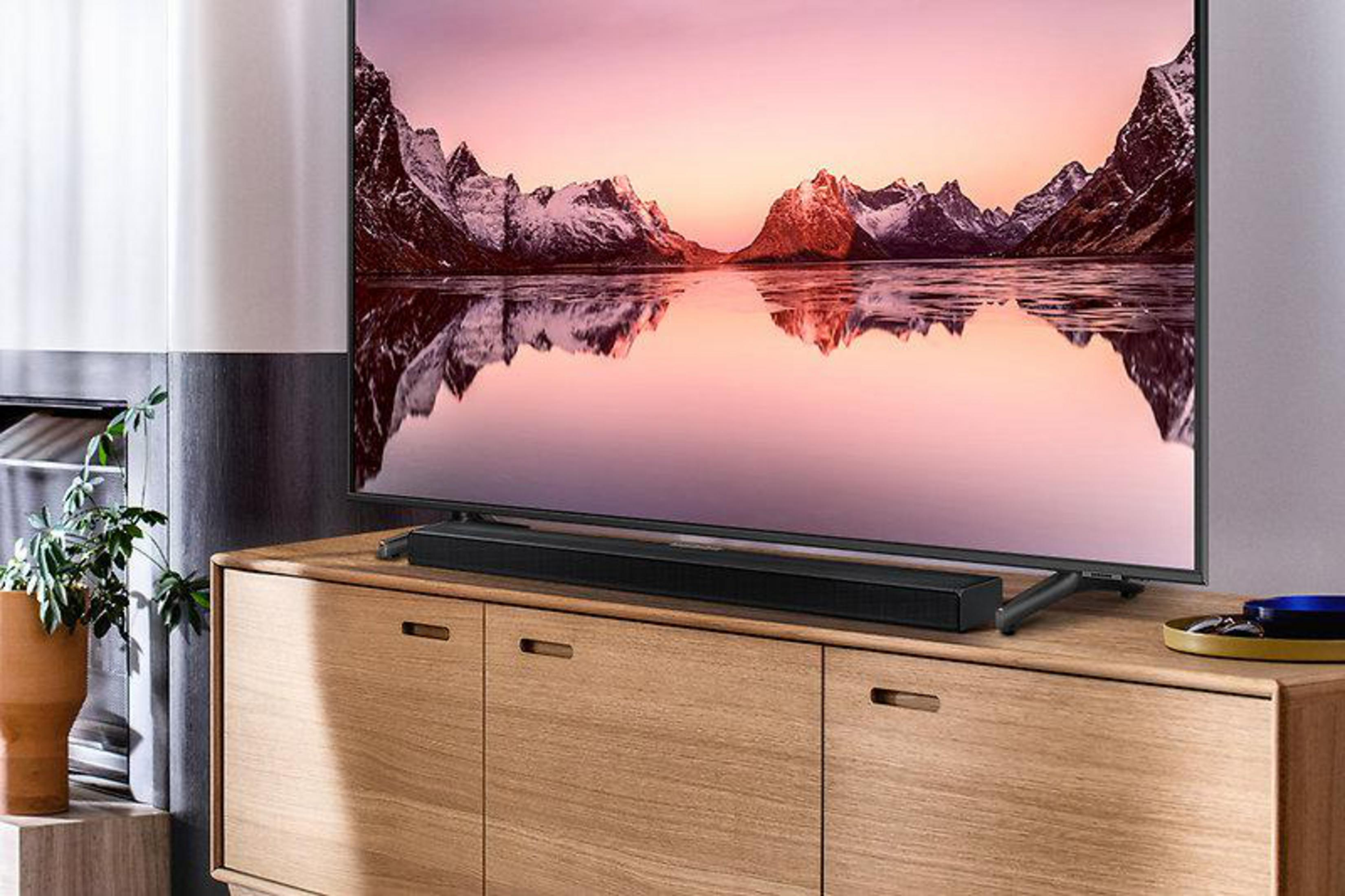 Fernseher auf einem Holzschrank mit Soundbar, Landschaft im Hintergrund und Pflanze.