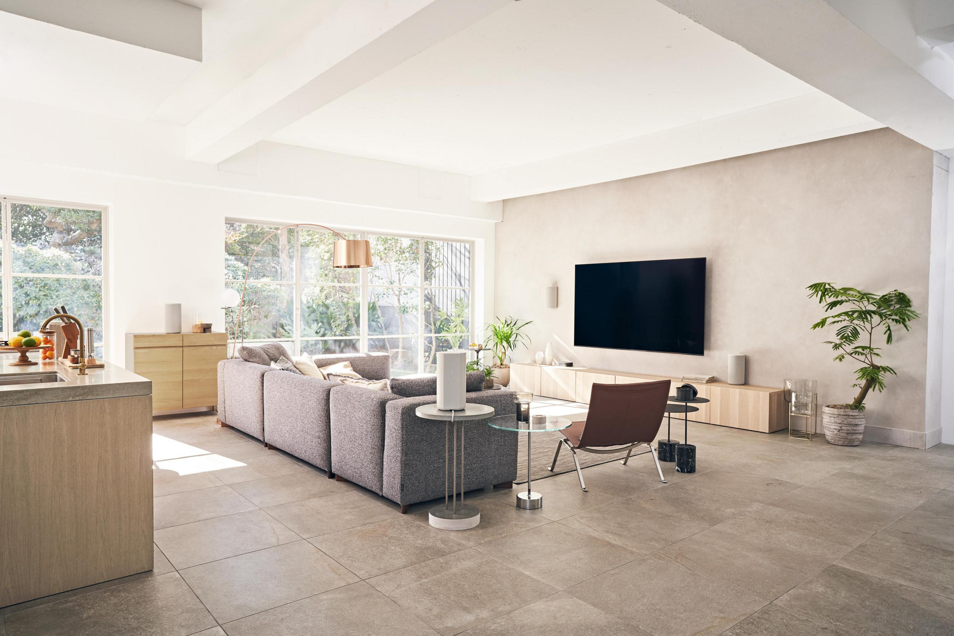 Modernes Wohnzimmer mit großem Sofa, Fernseher und Lautsprechern. Heller, offener Raum mit großen Fenstern.