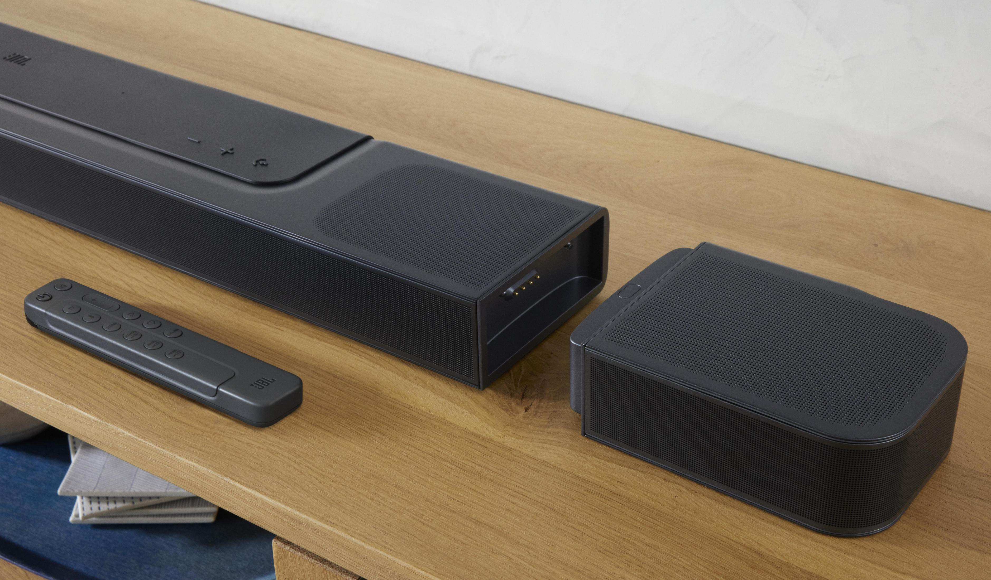 Eine schwarze Soundbar, ein Subwoofer und eine Fernbedienung auf einer Holzoberfläche. Die Soundbar hat Knöpfe.