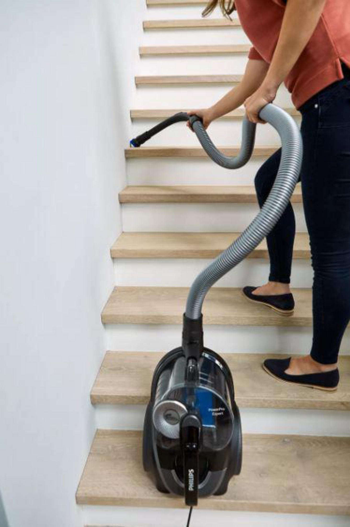 Una persona aspirando las escaleras. La aspiradora está en el escalón inferior.