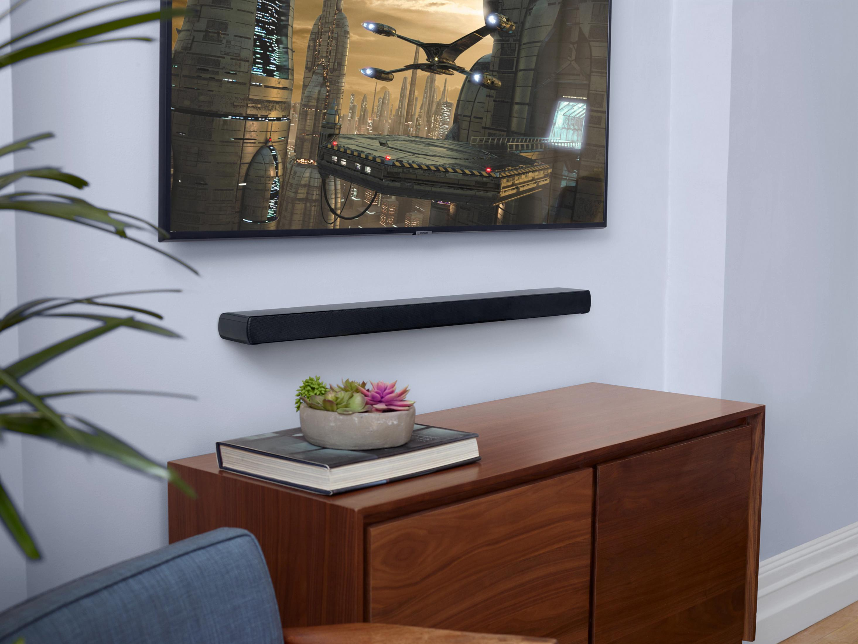 Ein Fernseher zeigt eine Szene mit einem Raumschiff. Darunter befindet sich eine Soundbar. Darunter steht ein Sukkulenten-Topf.