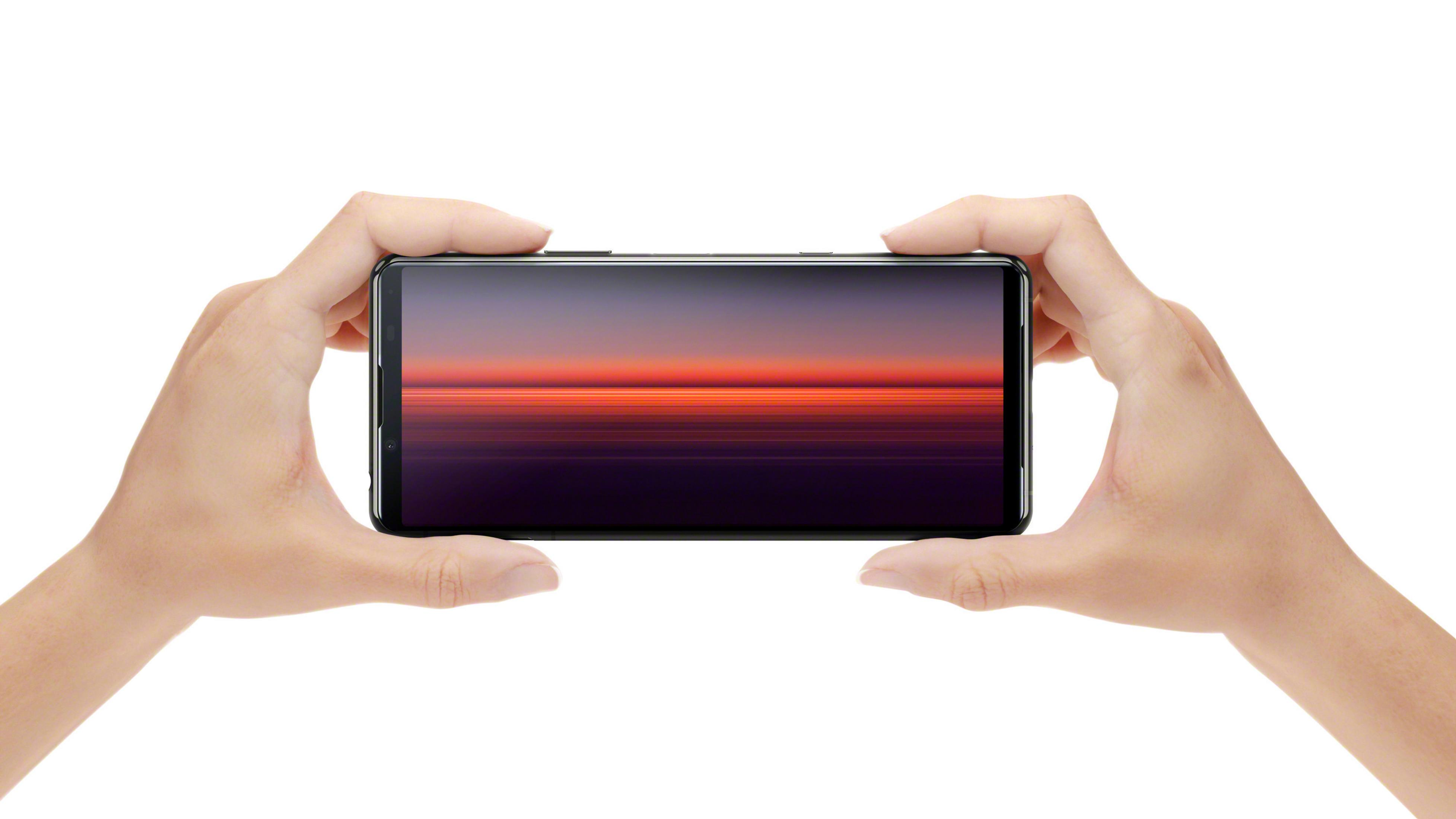 Dłonie trzymające telefon poziomo, wyświetlający obraz zachodu słońca.