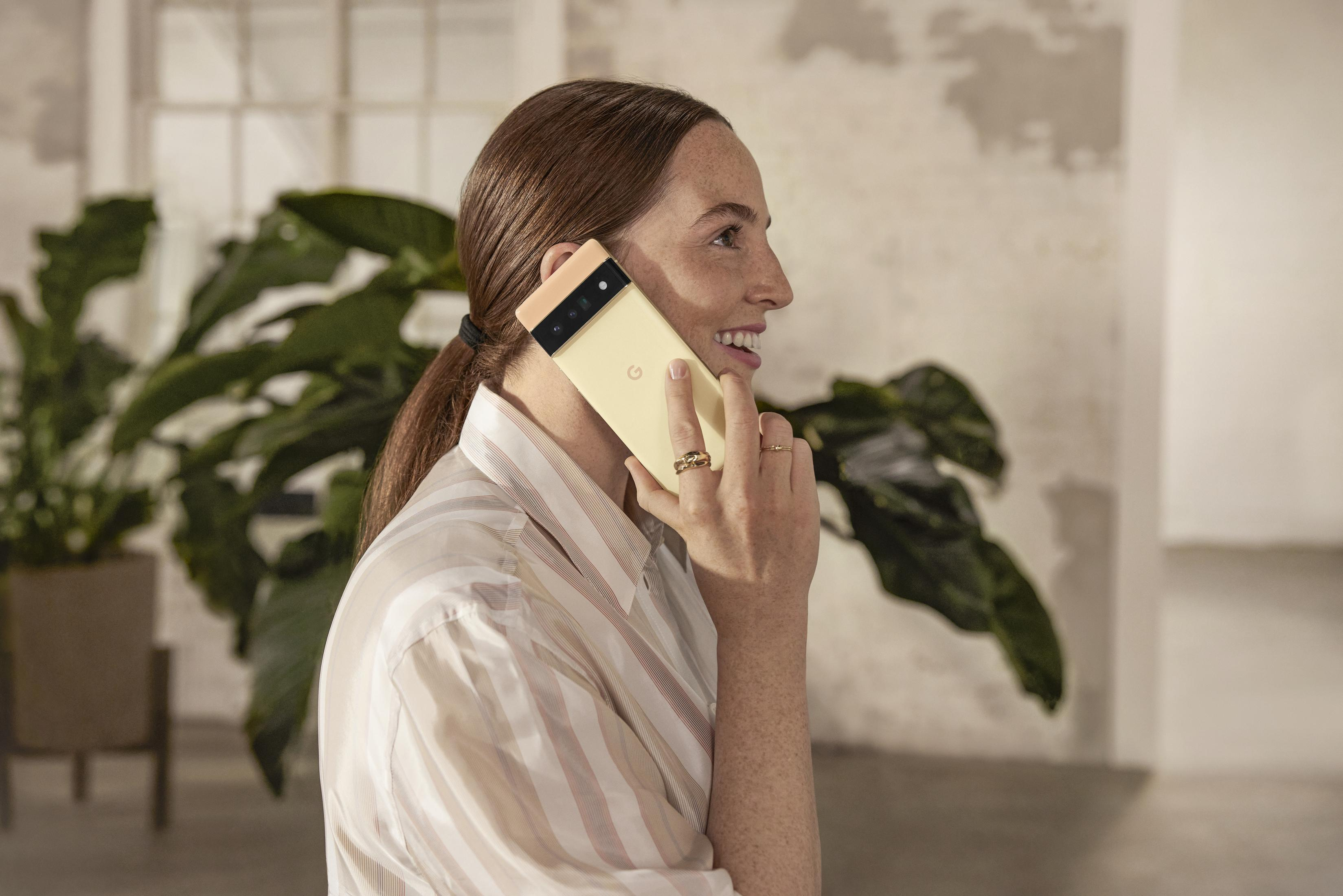 Kobieta z rudymi włosami trzymająca żółty telefon przy uchu, uśmiechnięta. Ma na sobie koszulę w paski.