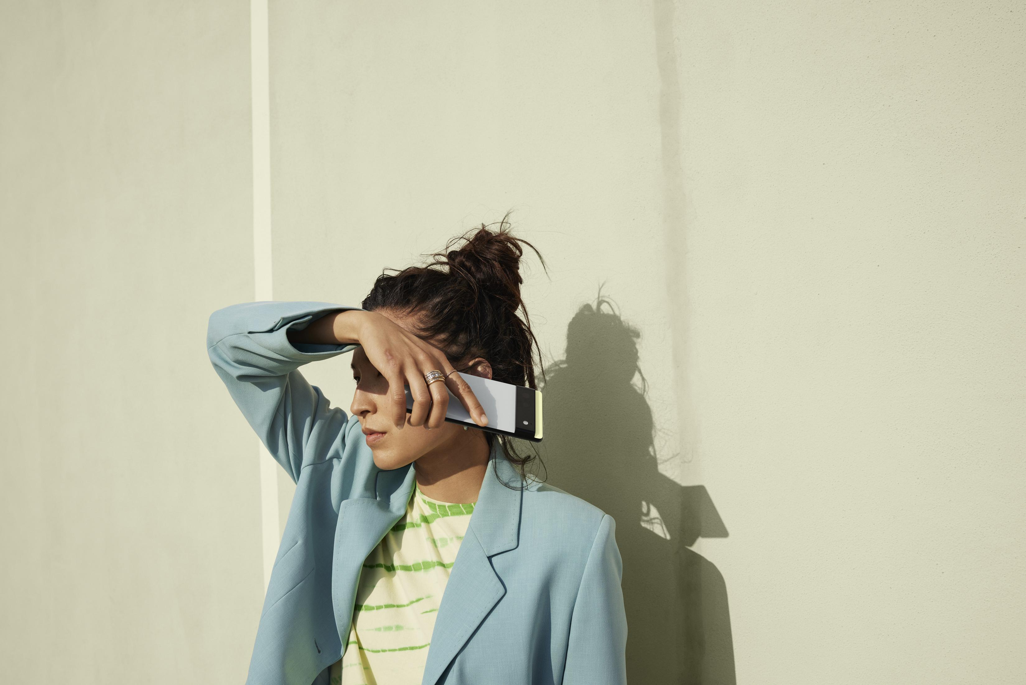 Frau, die ein Telefon hält und ihre Augen vor der Sonne schützt, mit beigem Wandhintergrund.