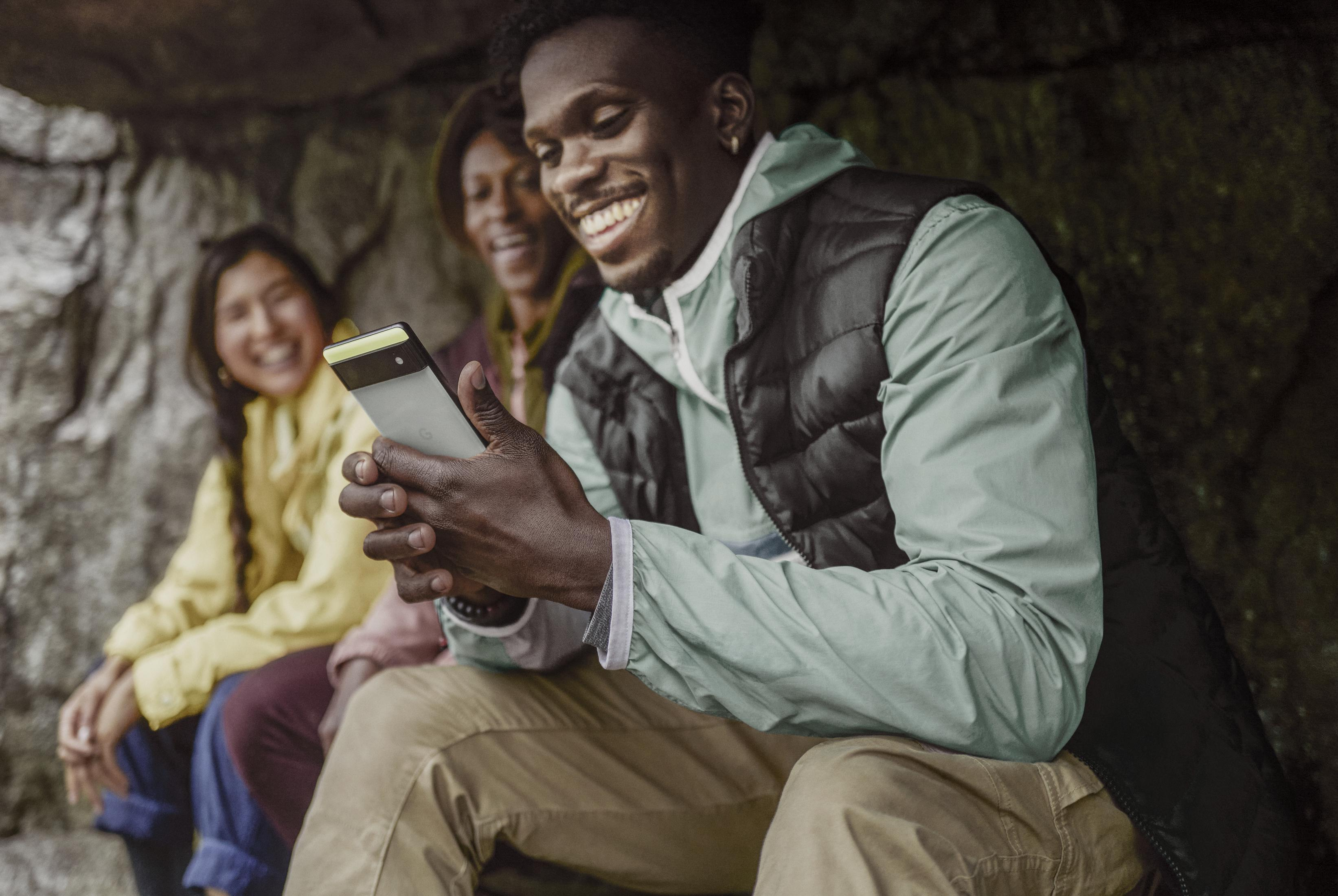 Drei lächelnde Personen schauen auf ein Telefon in der Natur.