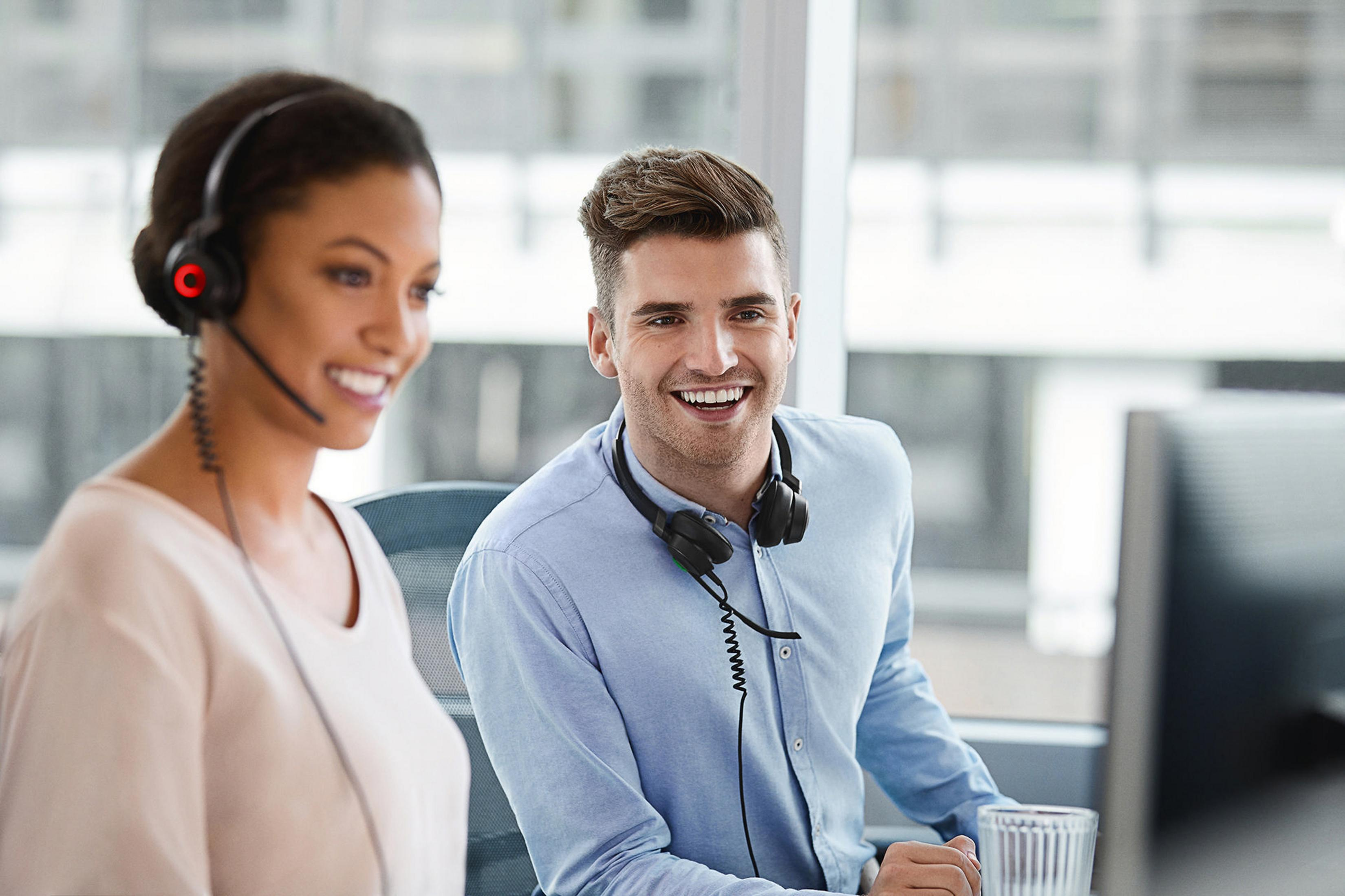 Mężczyzna i kobieta w pracy. Kobieta nosi zestaw słuchawkowy. Mężczyzna uśmiecha się do kamery.
