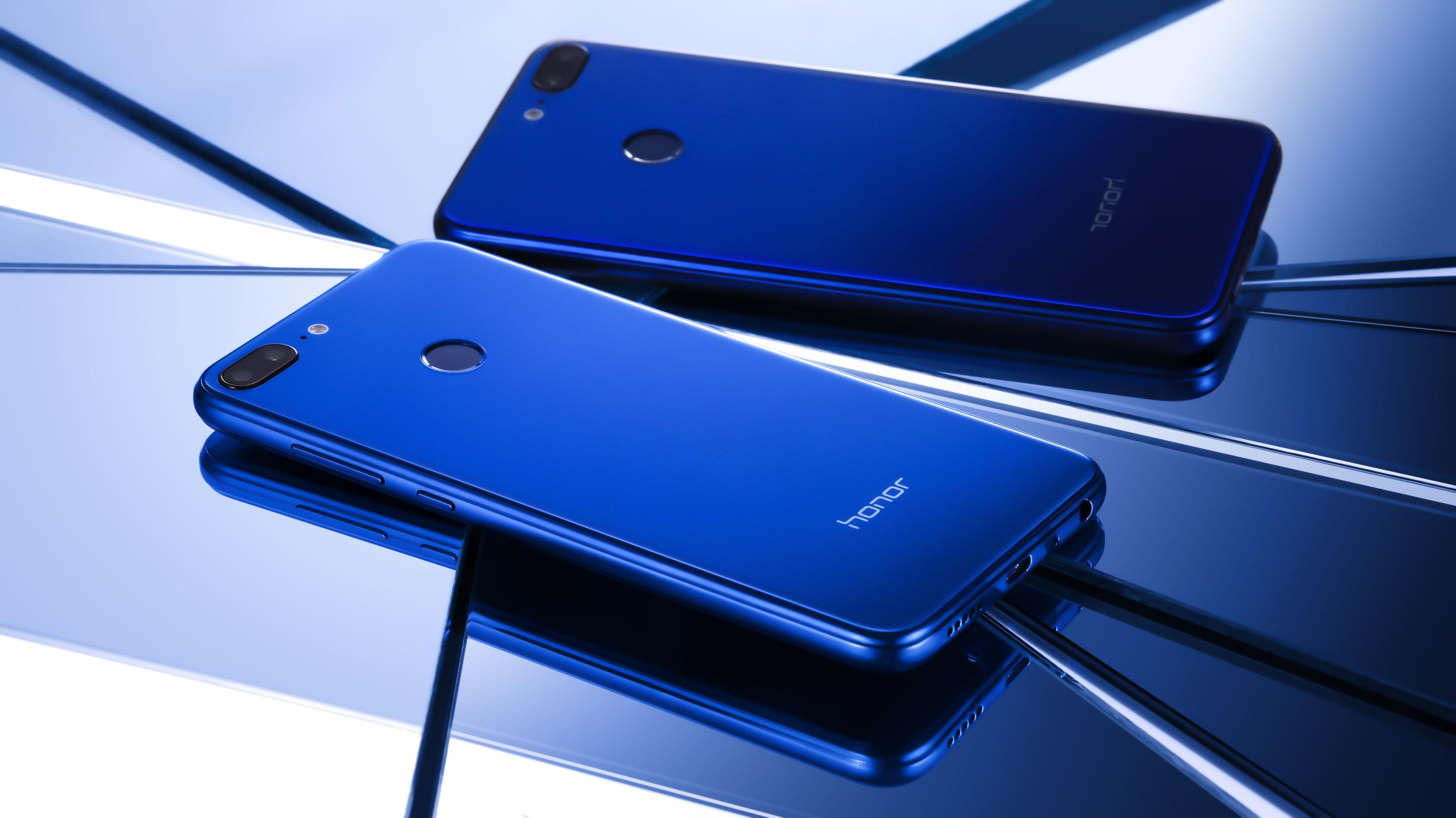 Zwei blaue Honor-Telefone auf einer reflektierenden Oberfläche. Die Rückseiten sind sichtbar.