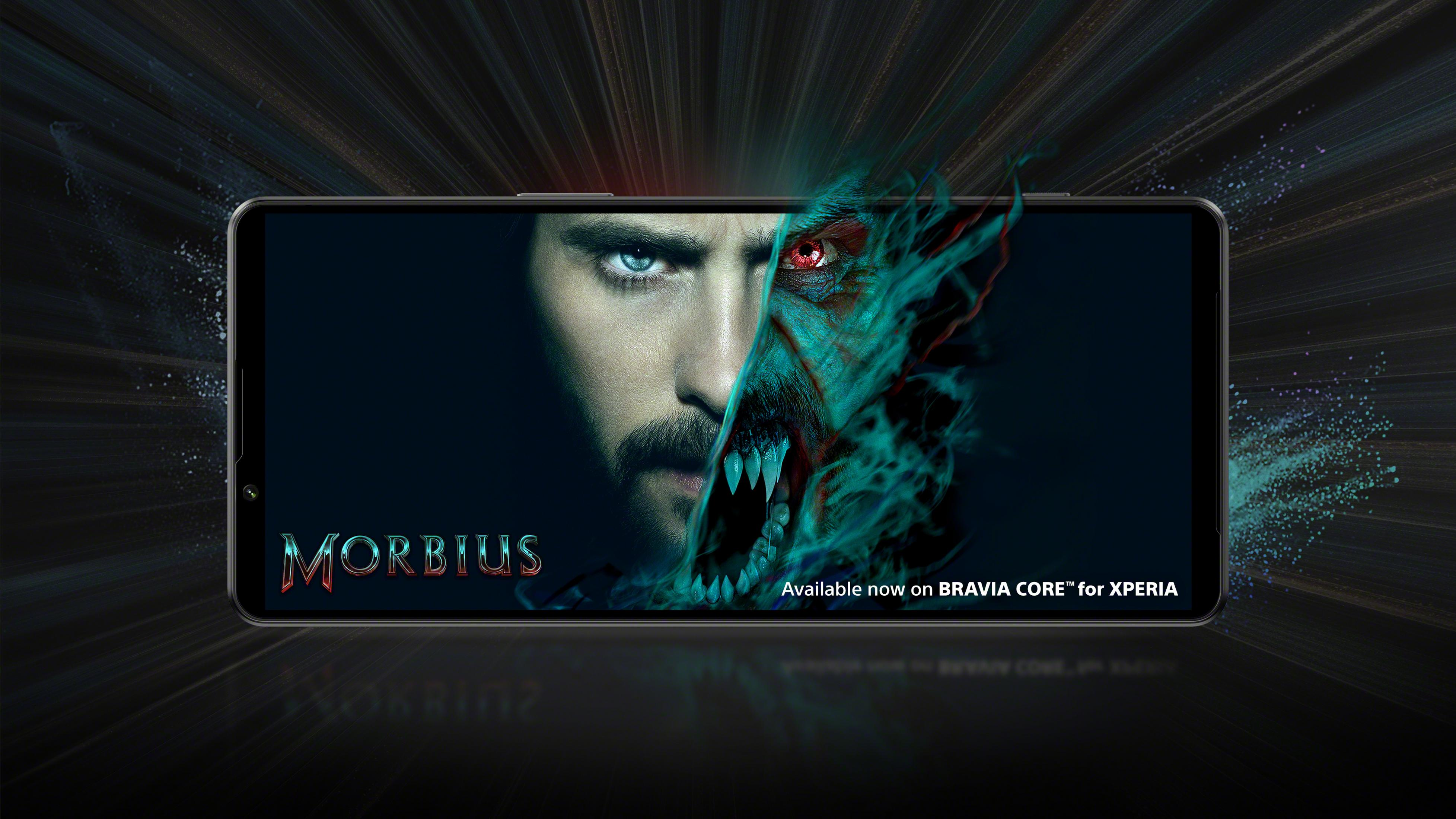 Ekran telefonu wyświetla plakat filmu Morbius. Tło jest ciemne i rozmyte.