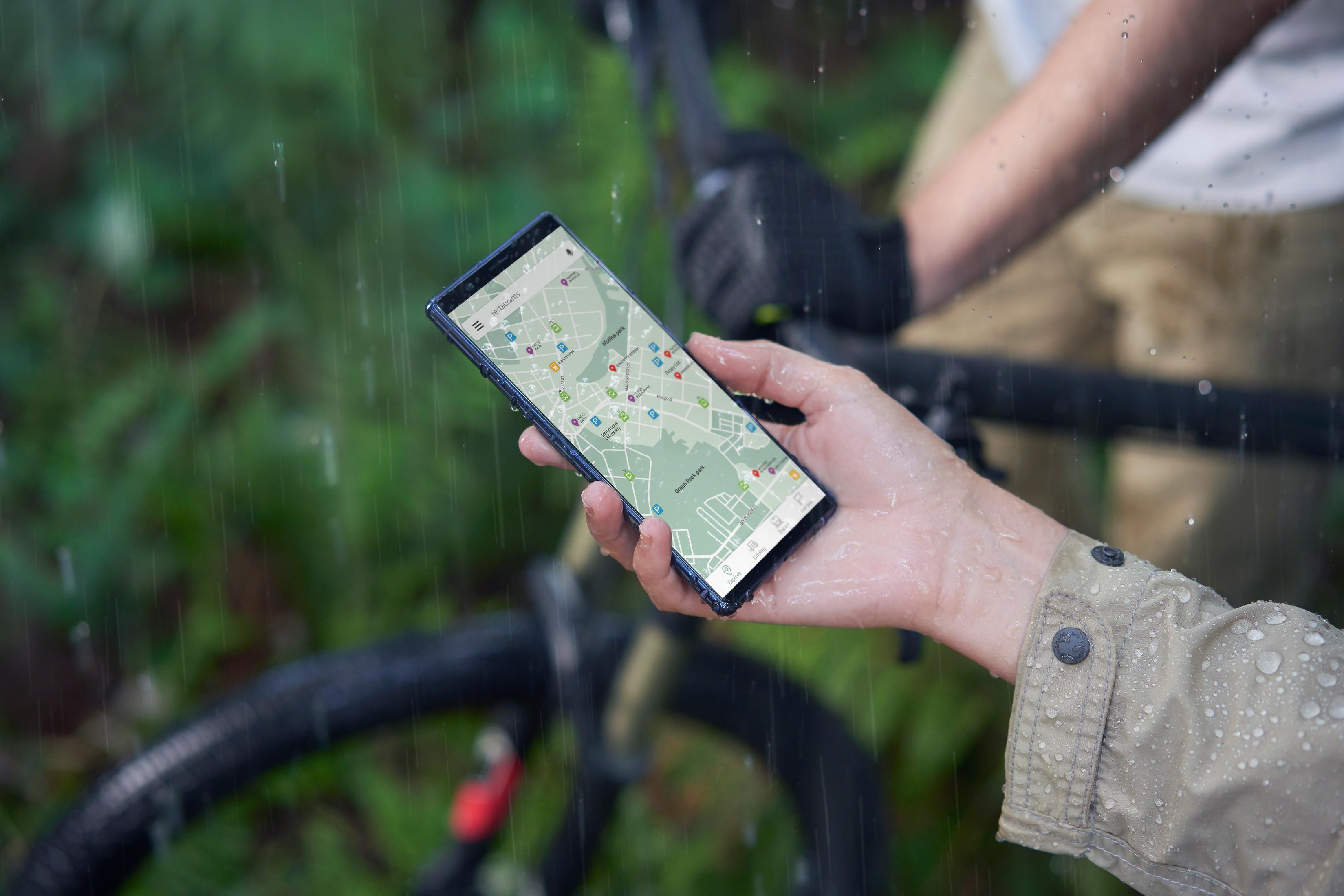 Osoba trzymająca telefon z otwartą aplikacją mapy podczas deszczu.