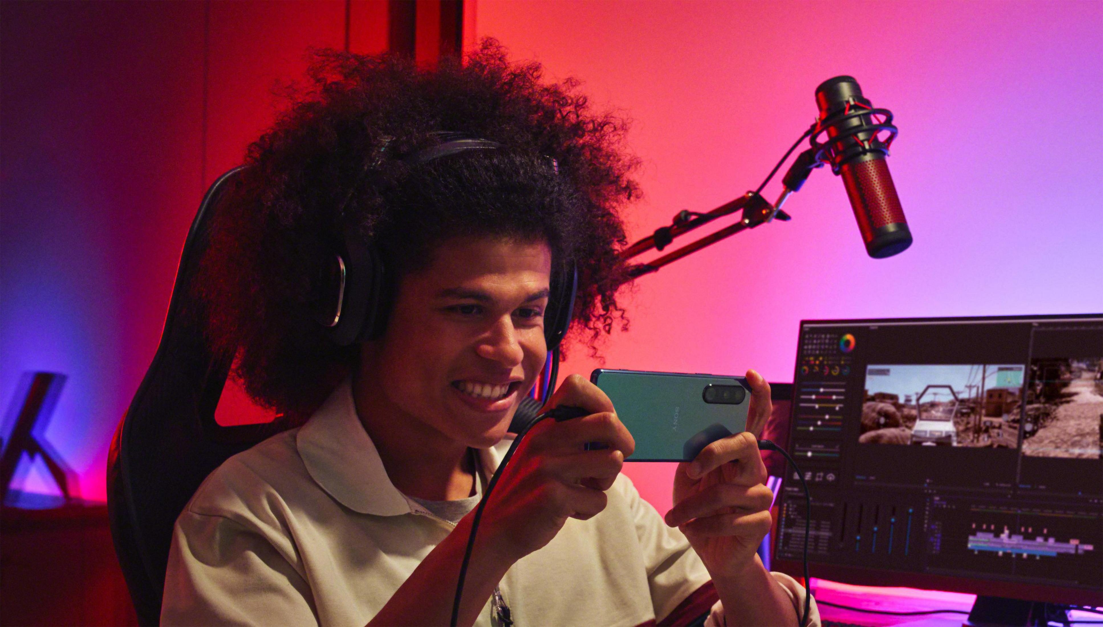 Mężczyzna gra na smartfonie, używając słuchawek i mikrofonu. Czerwone i niebieskie światła.