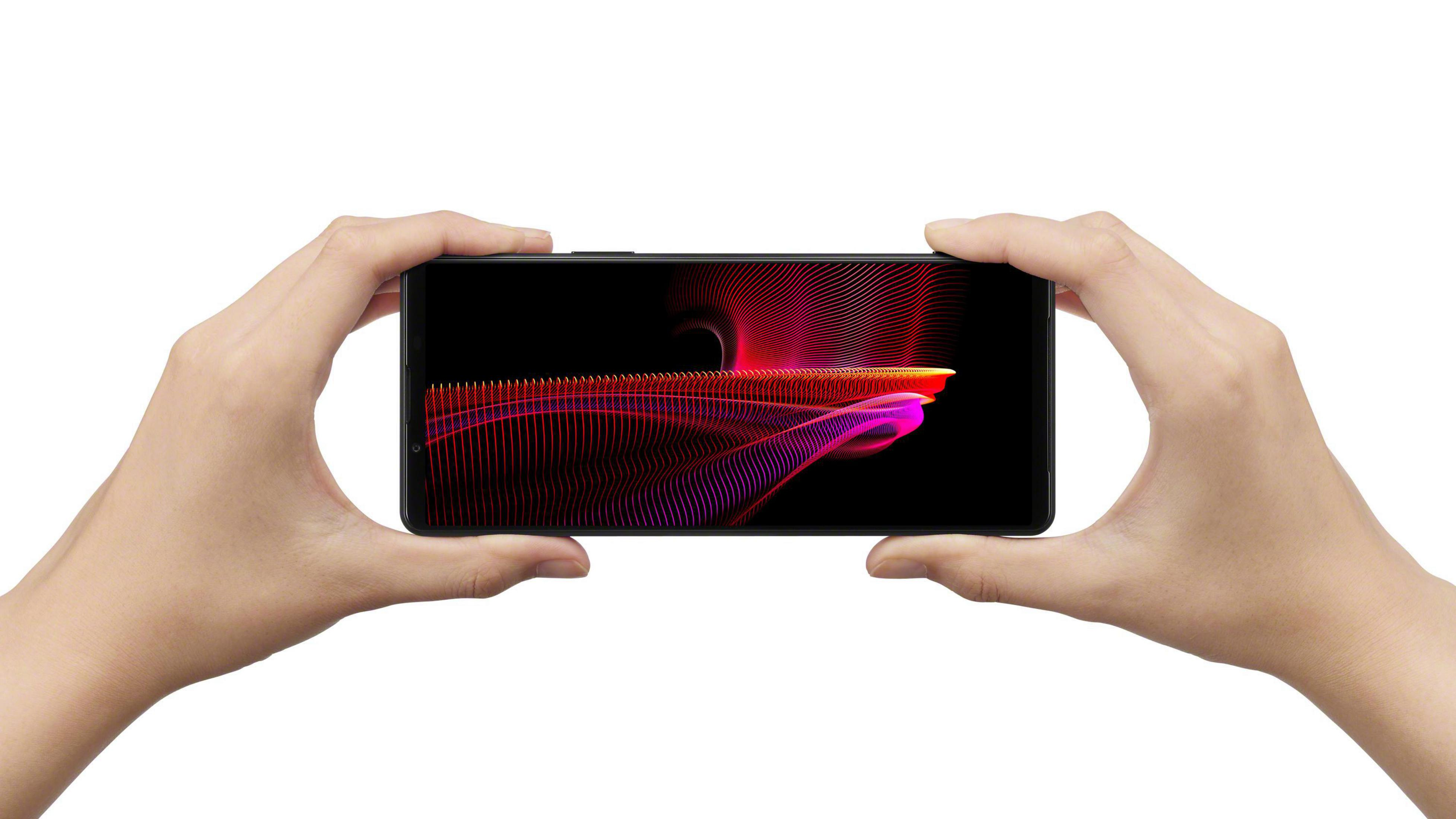 Hände halten ein Smartphone mit farbenfrohem abstraktem Design auf schwarzem Hintergrund.