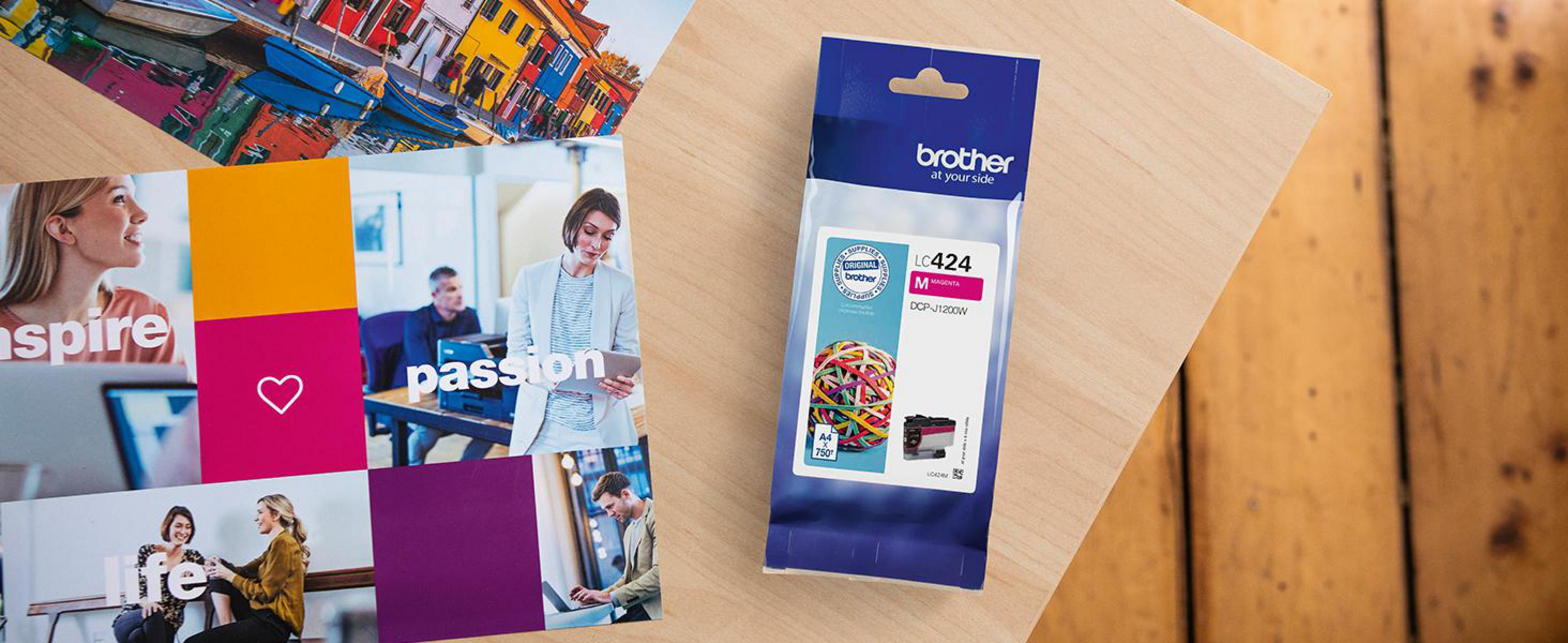 Houten tafel met kleurrijke marketingafbeeldingen, een Brother inktcartridge en promotiemateriaal.
