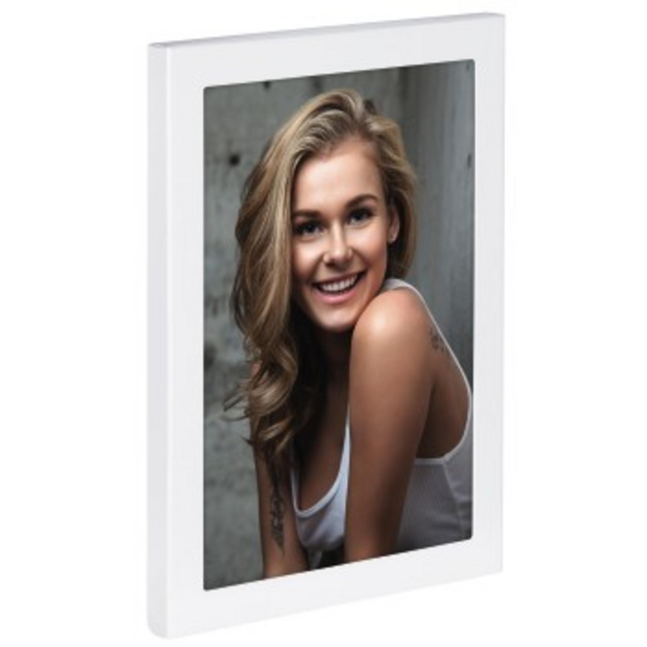 Ein gerahmtes Foto einer lächelnden Frau mit blonden Haaren, die ein weißes Tanktop trägt. Betonhintergrund.