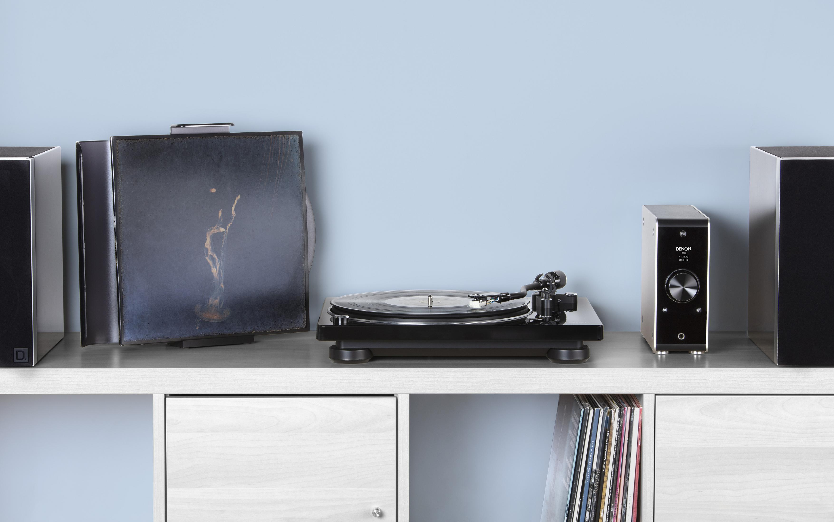 Un tocadiscos con un disco de vinilo y altavoces en una estantería blanca contra una pared azul.