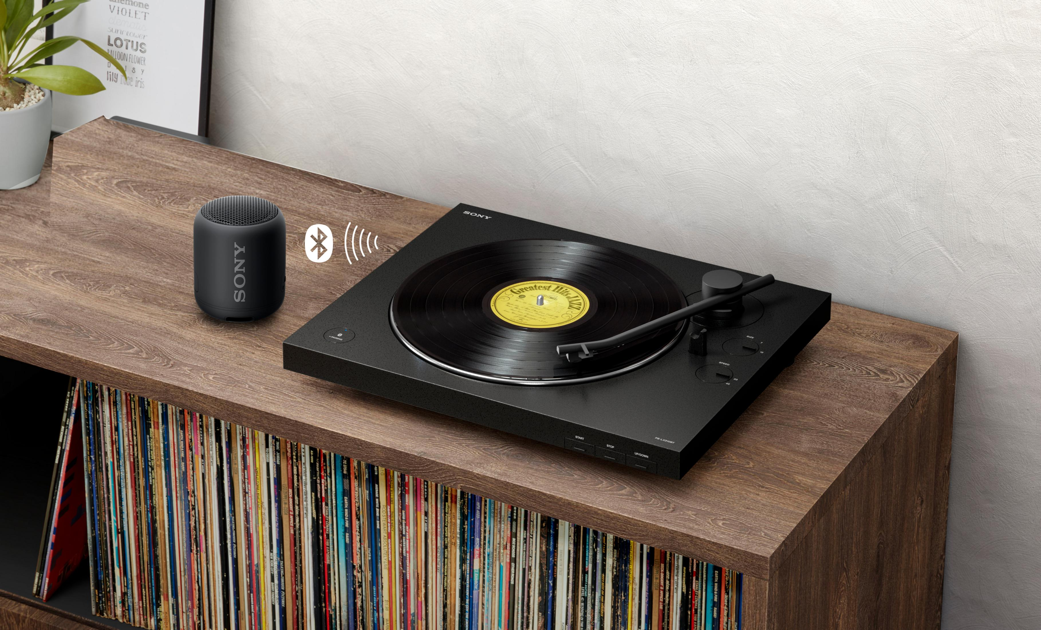 Un tocadiscos negro está en un estante de madera con discos. Un pequeño altavoz está al lado del tocadiscos.