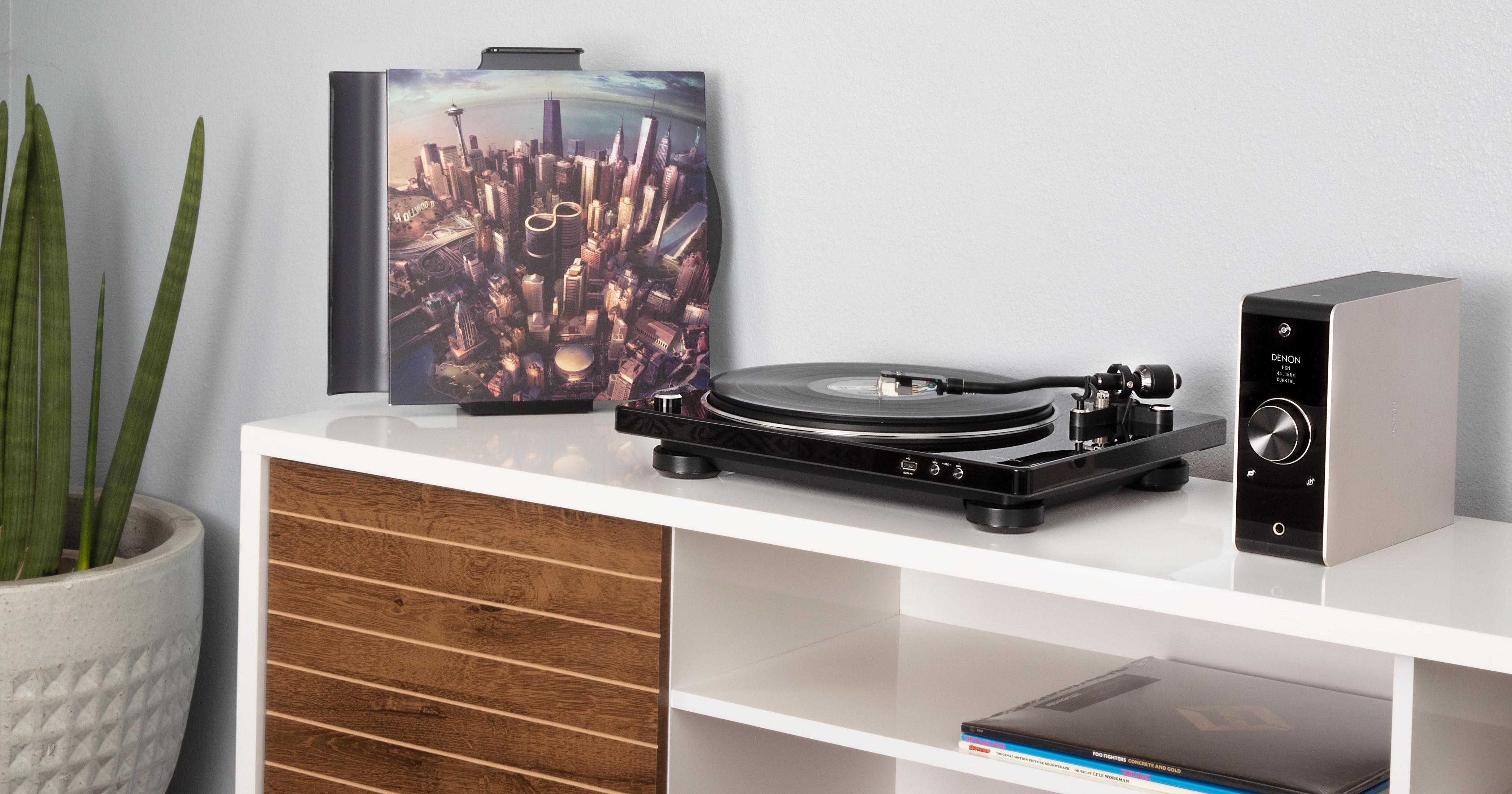 Plattenspieler mit Schallplatte, Albumcover und Denon-Soundsystem auf einem weißen Holzschrank.