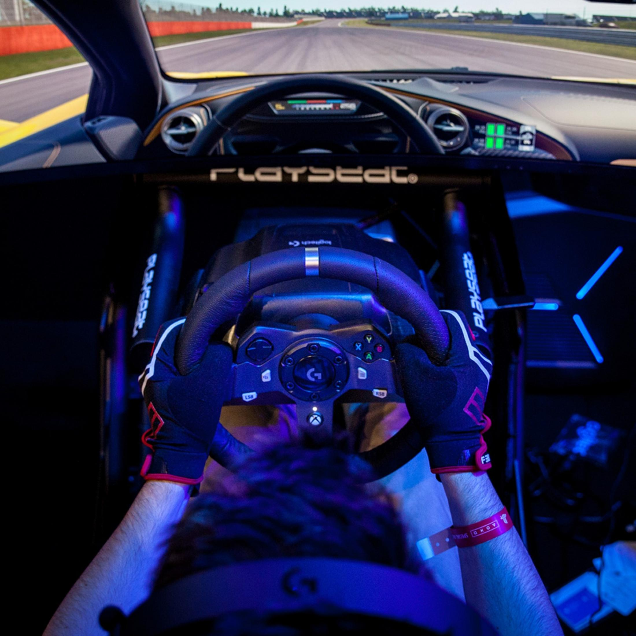 Eine Person mit Handschuhen hält ein Lenkrad in einem Autosimulator.