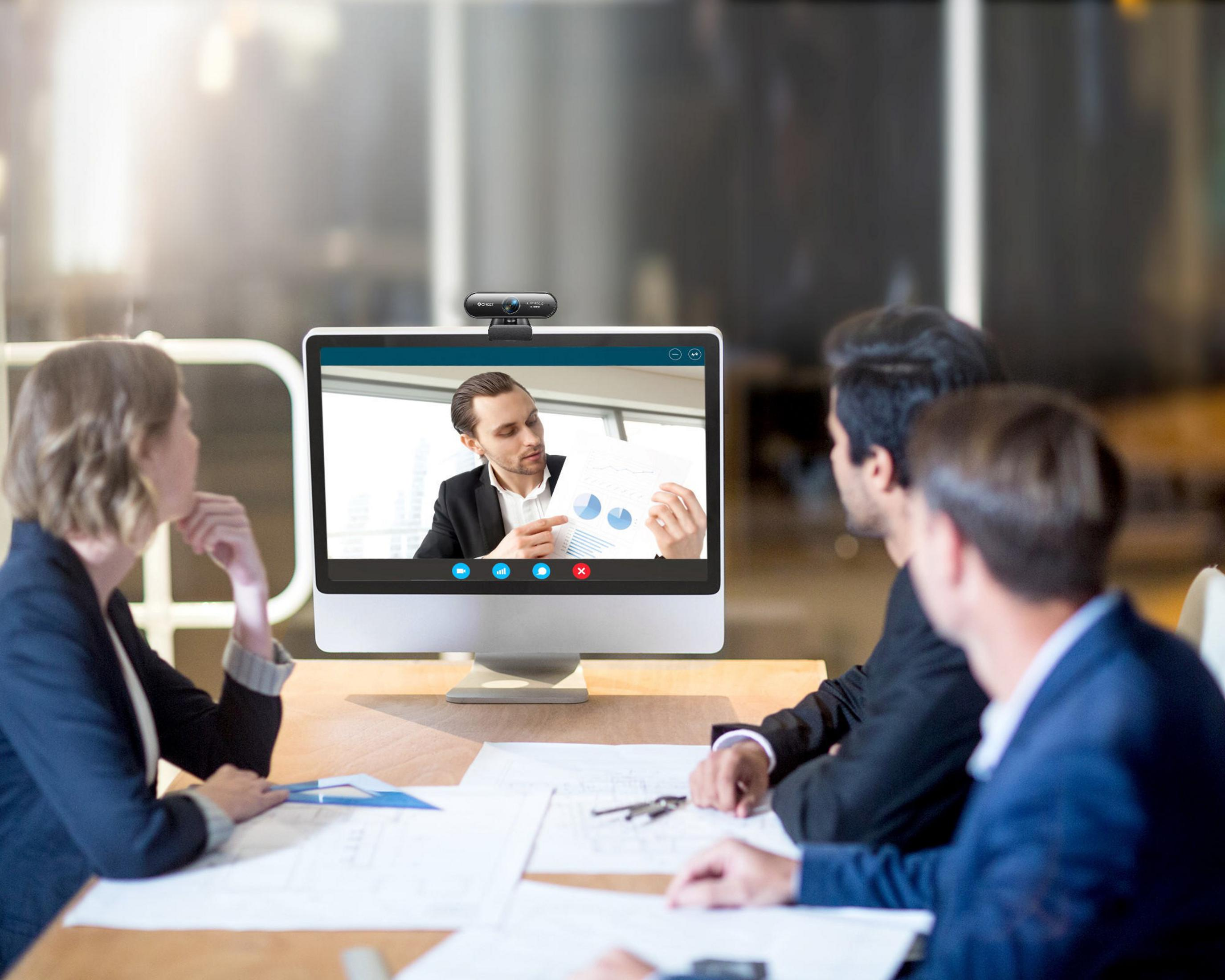 Besprechung mit Videoanruf. Leute vor einem Monitor. Mann präsentiert Daten.