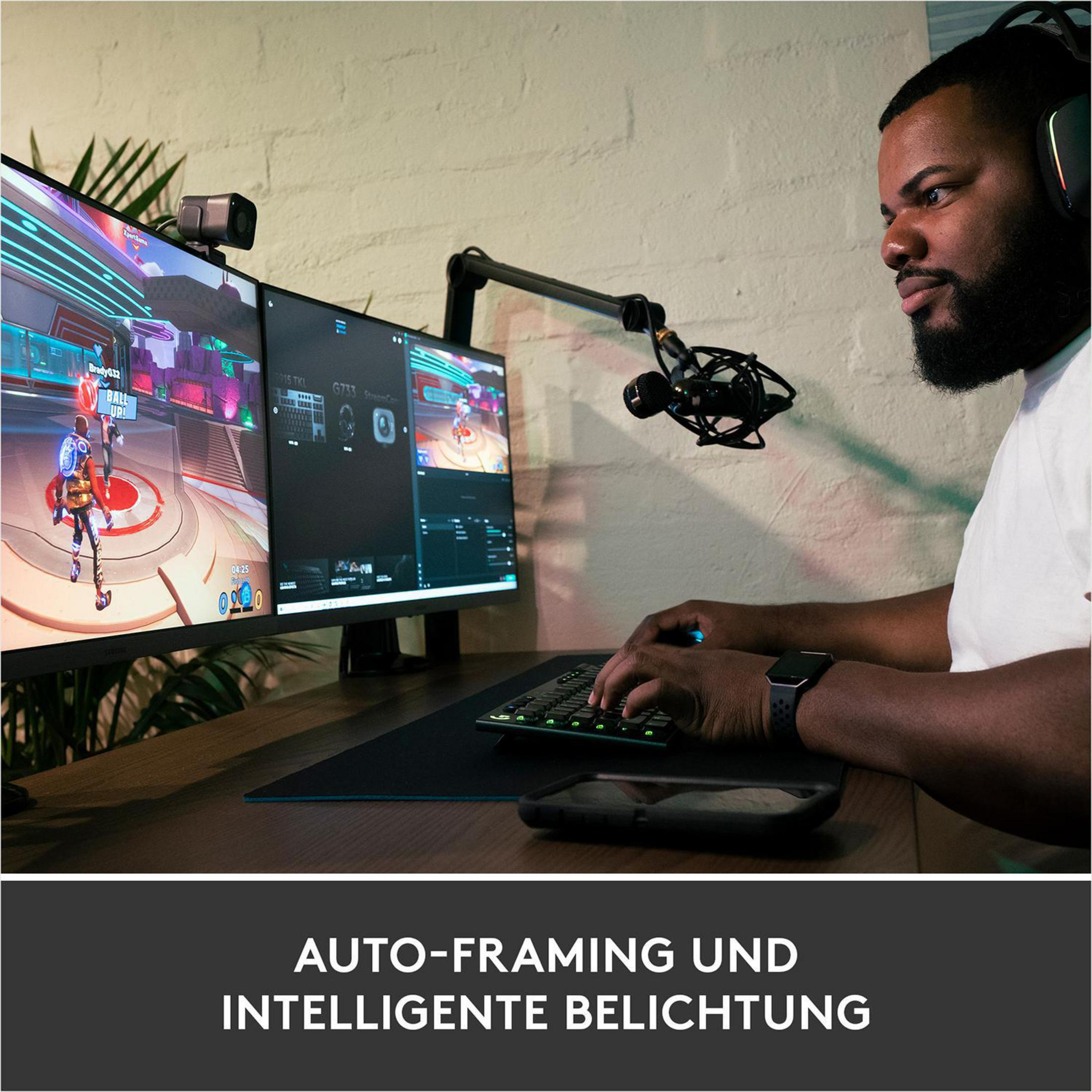 Mężczyzna gra z dwoma monitorami, mikrofonem i klawiaturą. Tekst na dole mówi o automatycznym kadrowaniu.