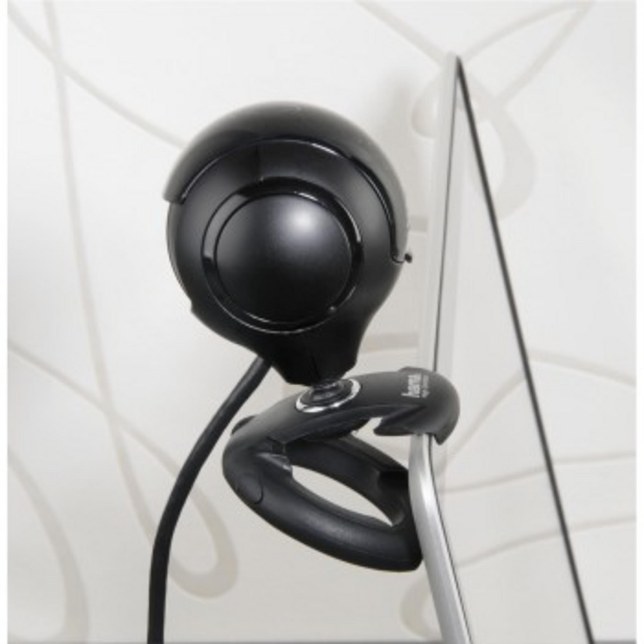 Una webcam nera è agganciata a un laptop. La webcam è rotonda e ha una lente al centro.