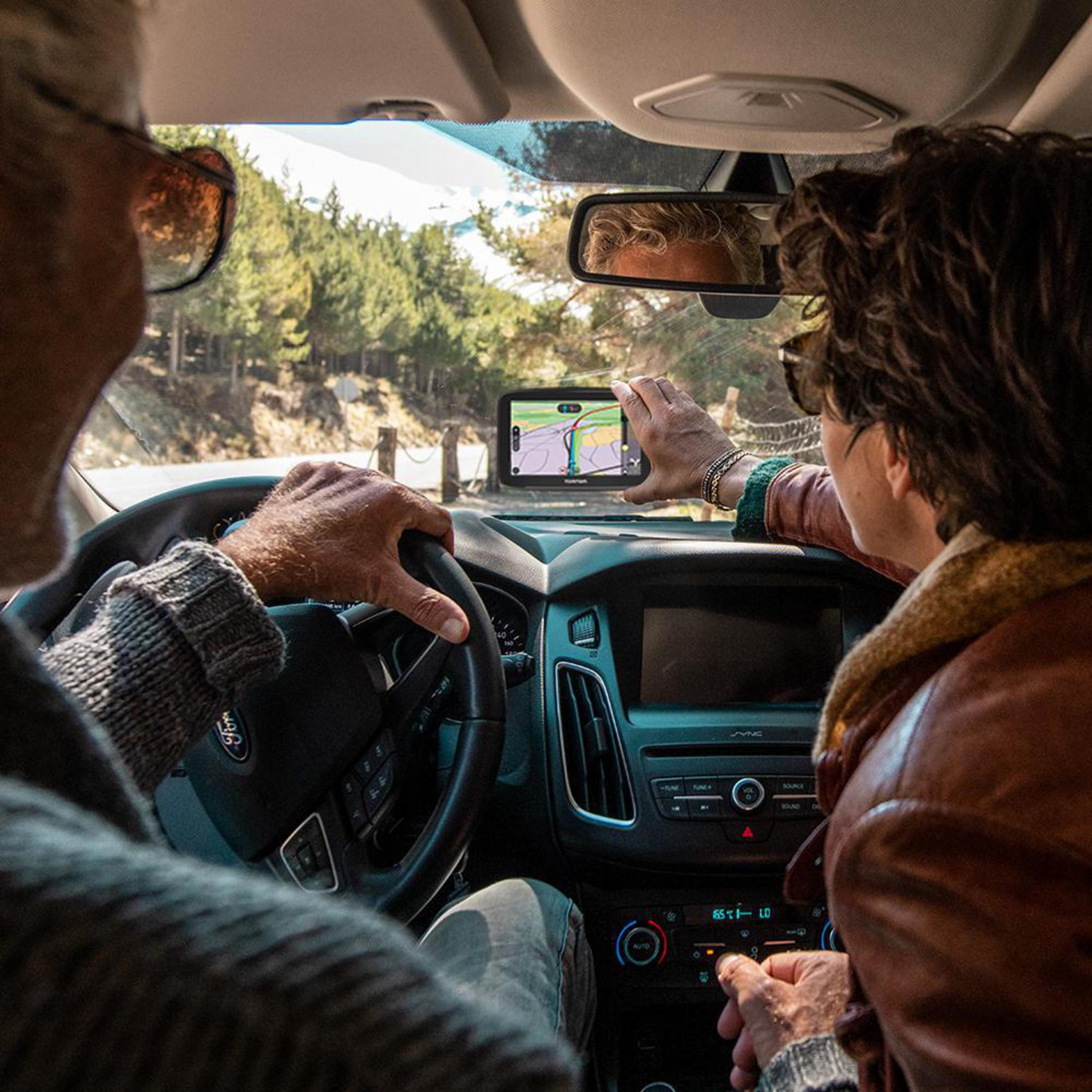 Zwei Personen in einem Auto, eine hält ein GPS-Gerät, fahren durch einen Wald.