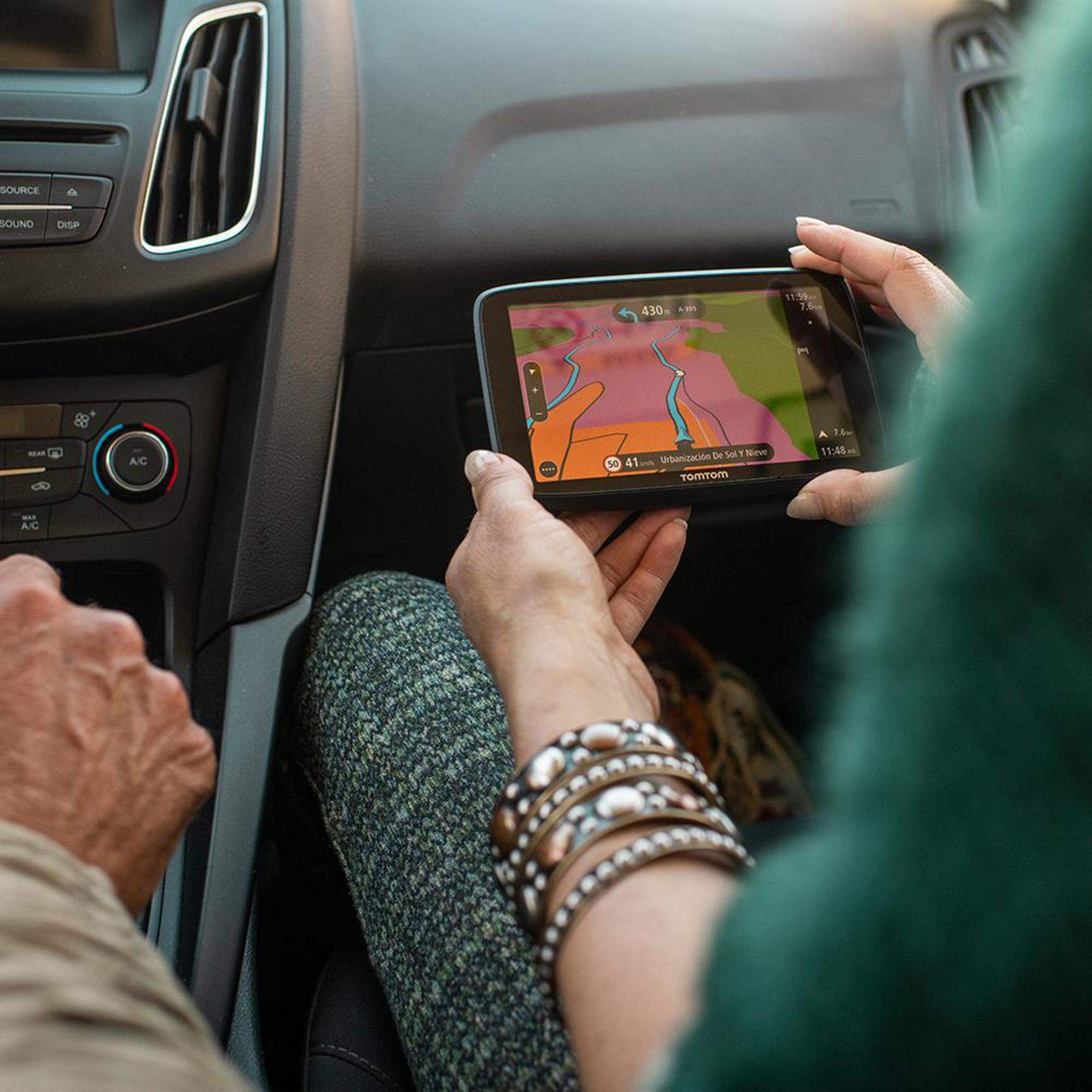 Hände halten ein GPS-Gerät im Auto mit einer Karte. Der Hintergrund ist der Innenraum des Autos.