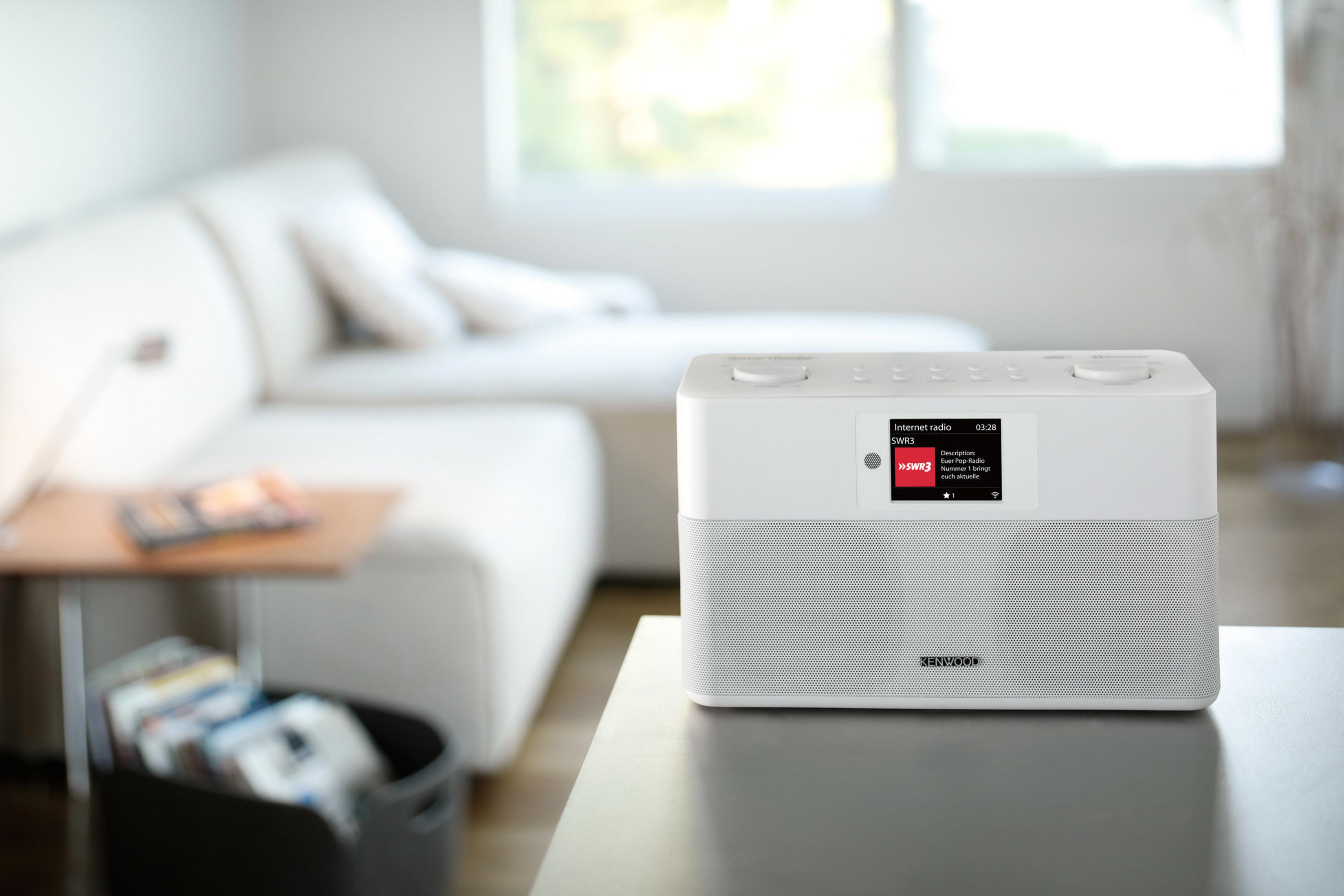 Białe radio internetowe Kenwood na stole. Biała sofa i okno w tle.