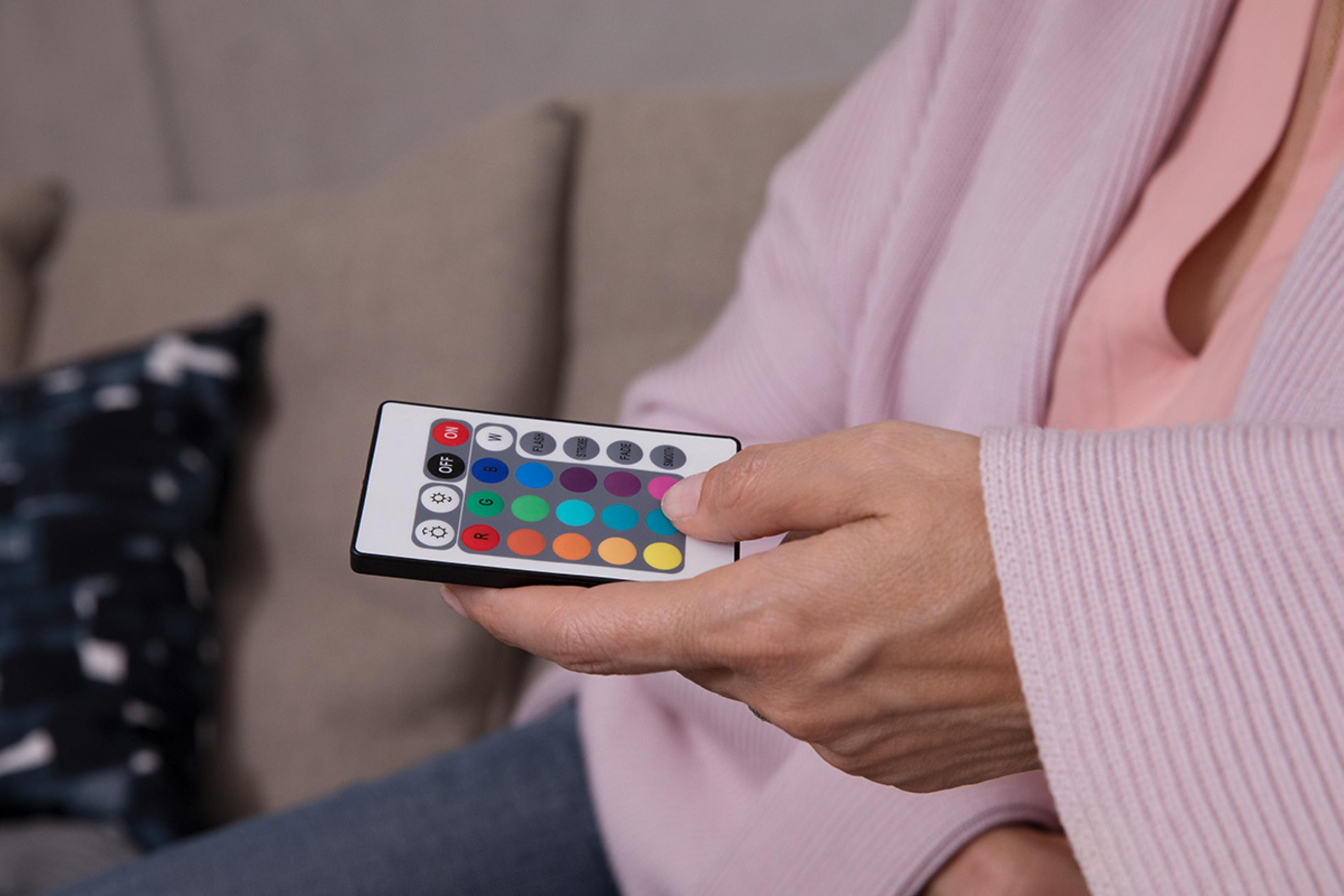 Mano che tiene un telecomando con pulsanti colorati, persona in abiti rosa.