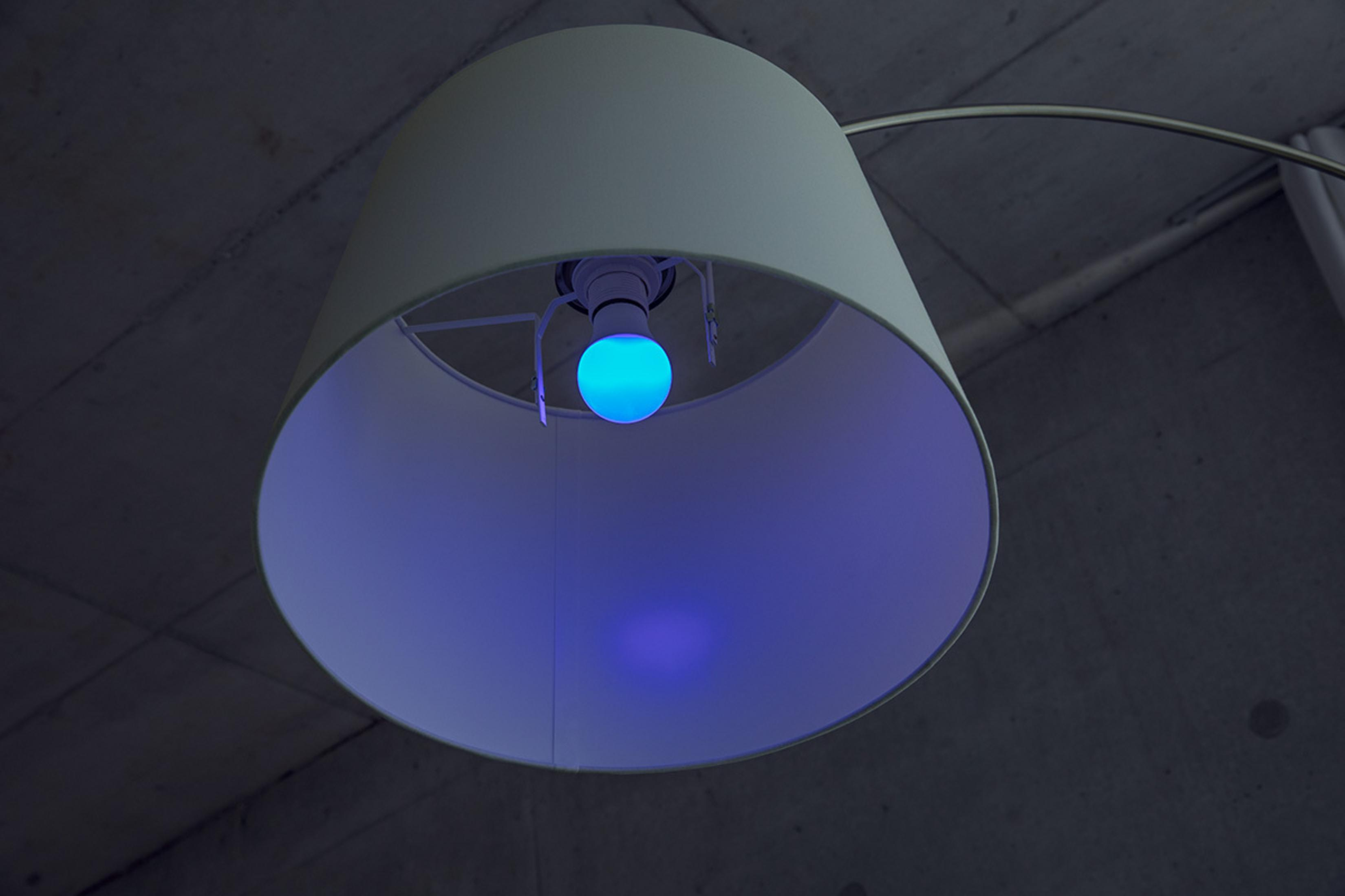 Una lampada con paralume bianco e una lampadina blu che emette luce blu.