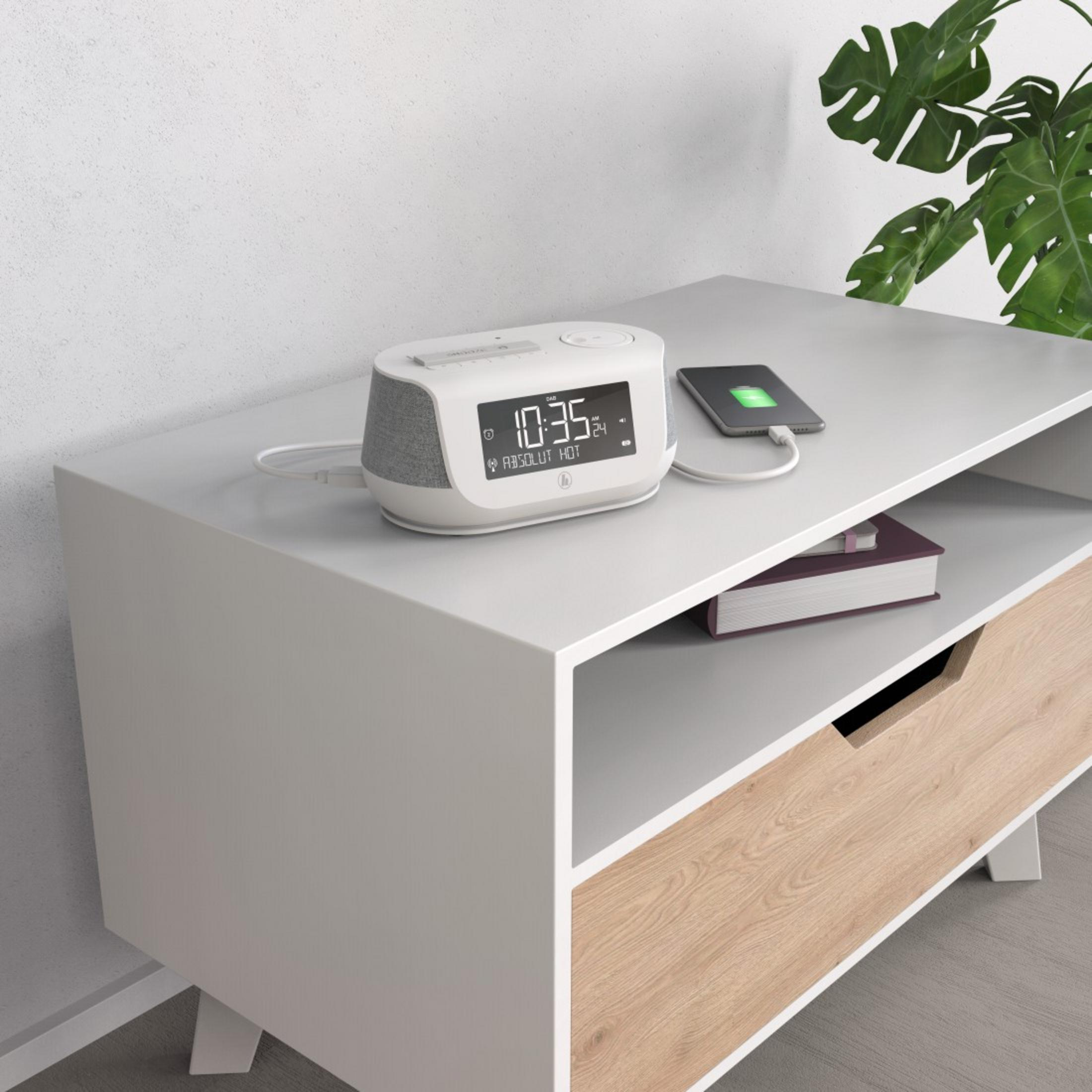 Biała szafka nocna z zegarem, telefonem, książką i rośliną.