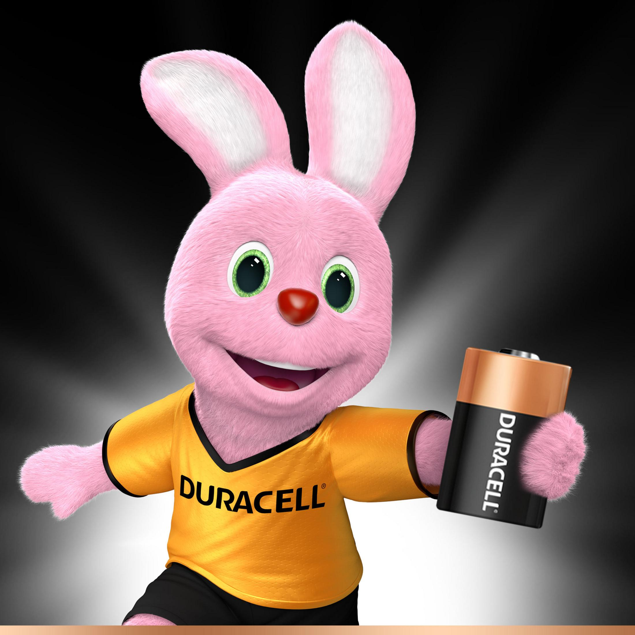 Różowy królik Duracell trzymający baterię Duracell. Królik uśmiecha się i nosi żółtą koszulkę.