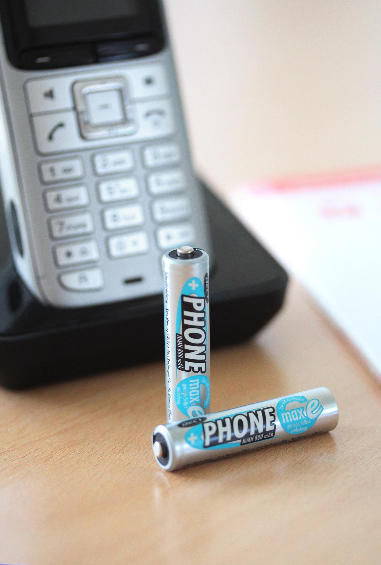 Zwei silberne AA-Batterien und eine schnurlose Telefonbasis.