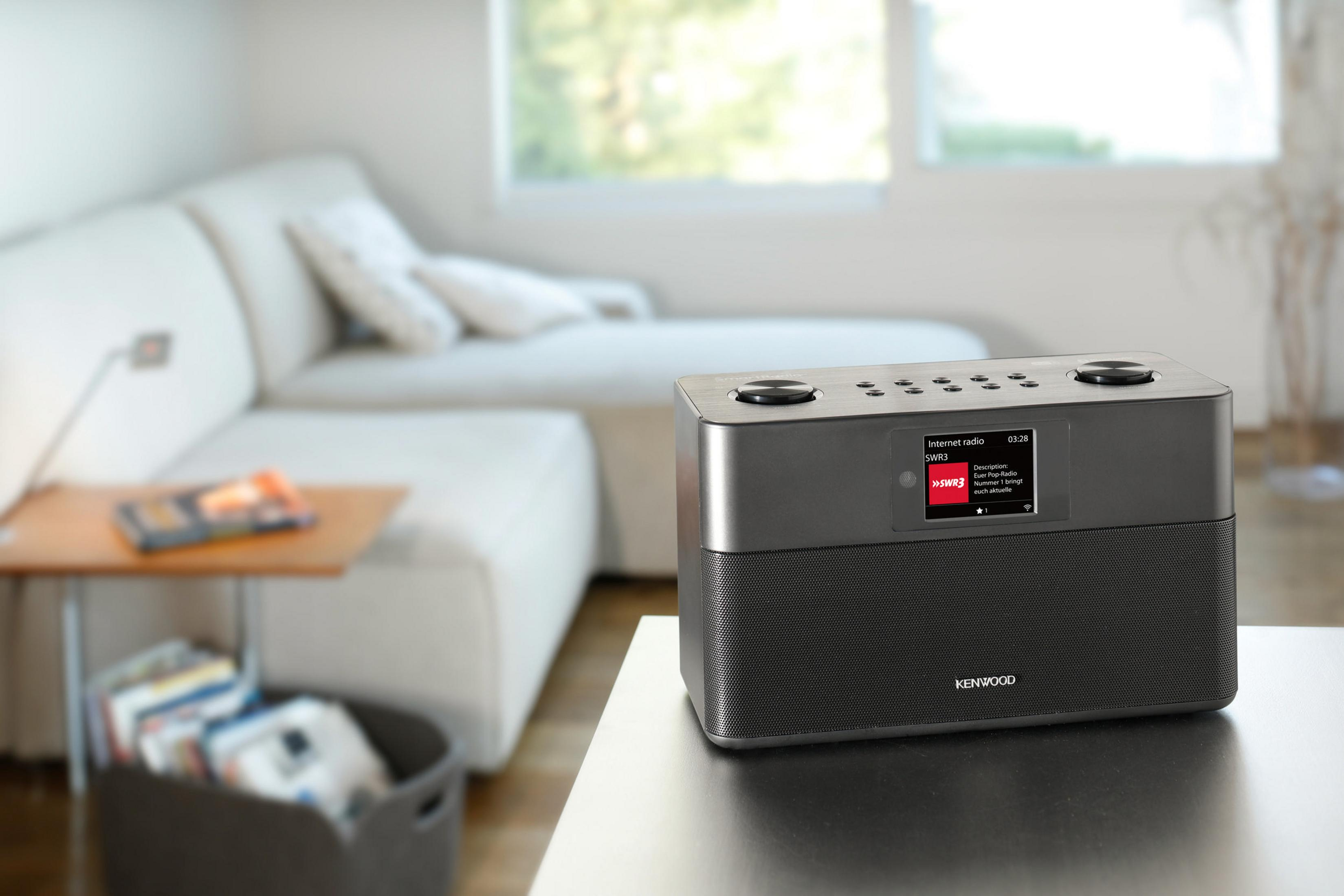 Czarno-szare radio na stole, z sofą w tle.