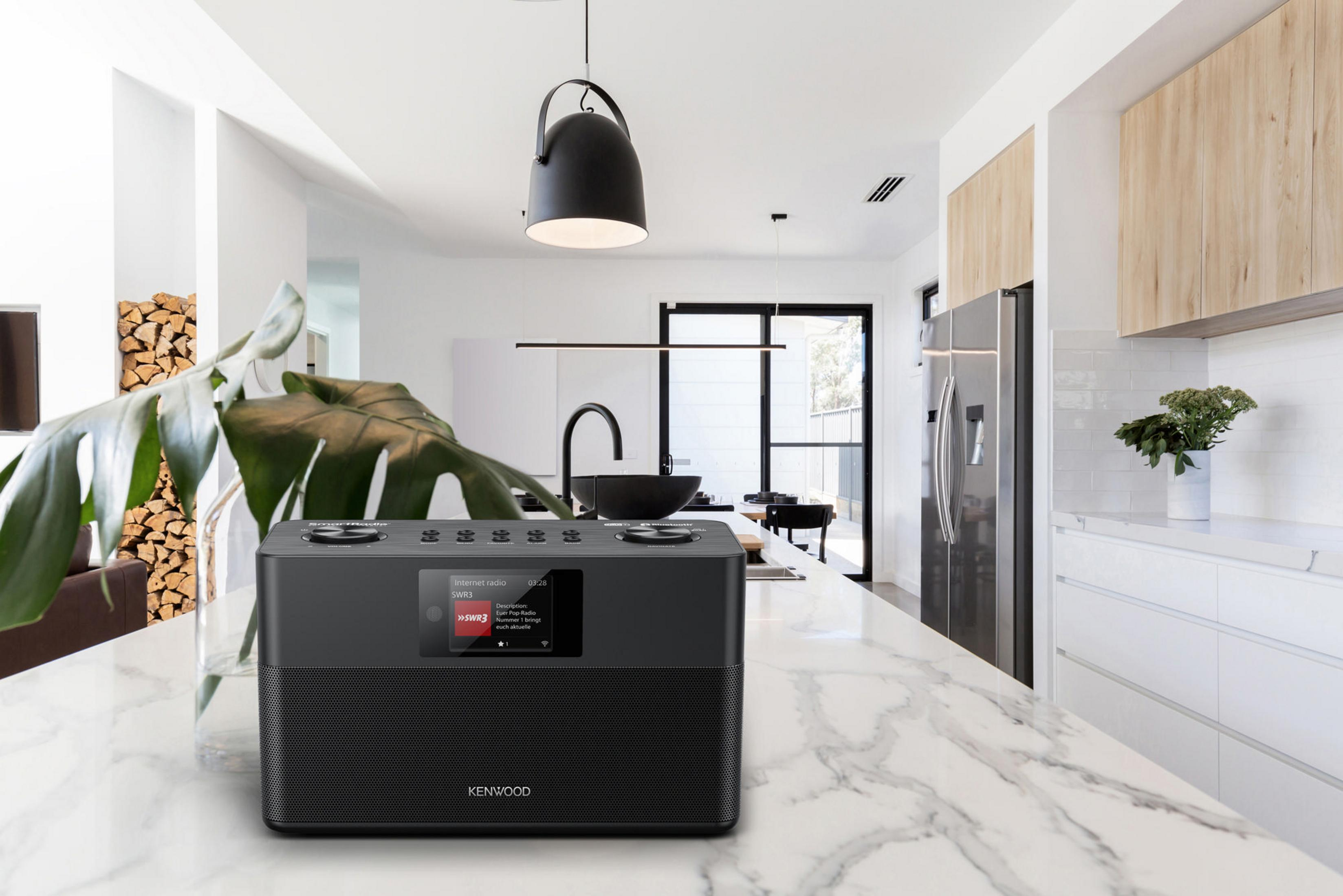 Czarny radio Kenwood na białym blacie. W tle kuchnia z białymi ścianami.