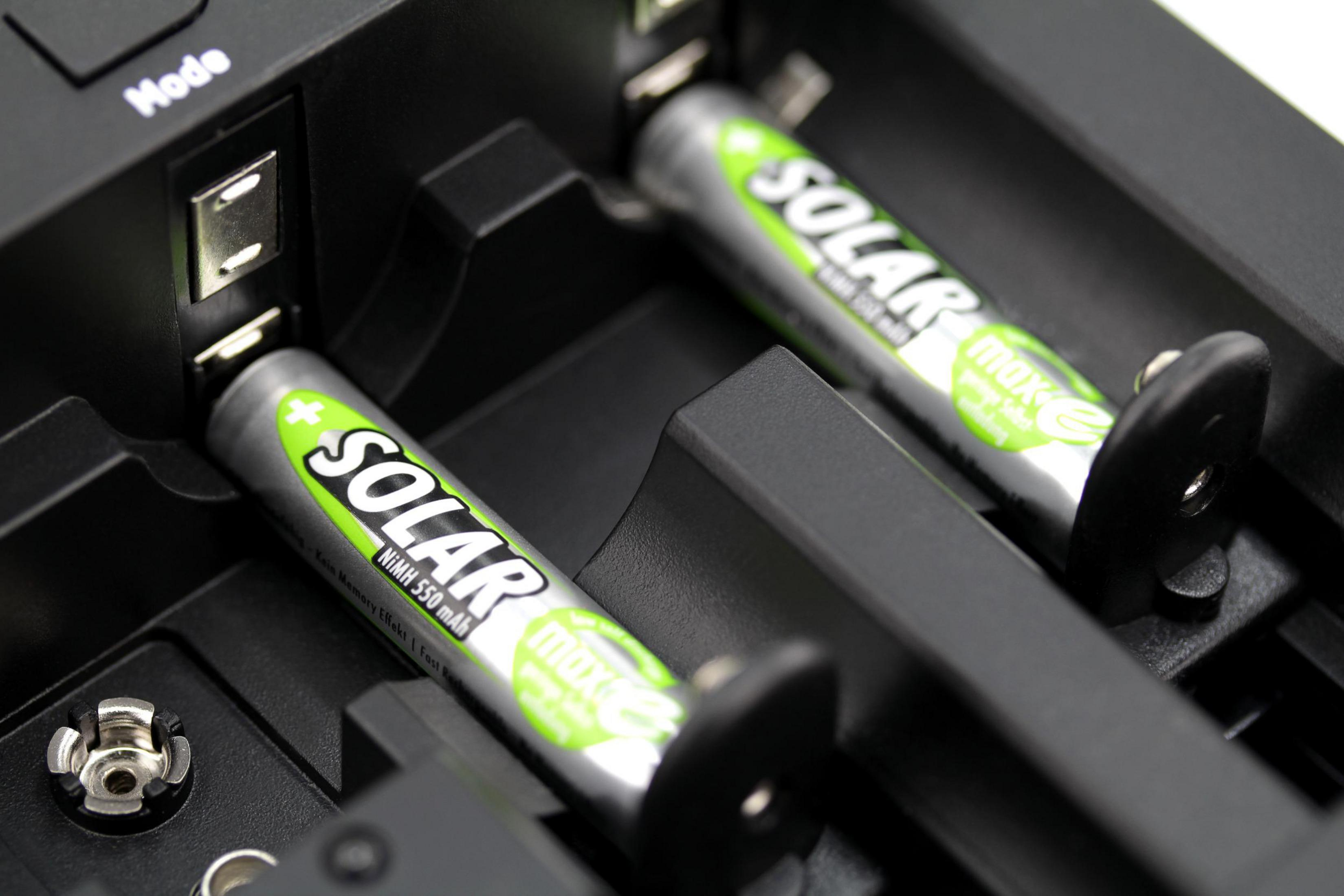 Due batterie AA in carica in un caricabatterie nero. Testo verde e bianco sulle batterie.