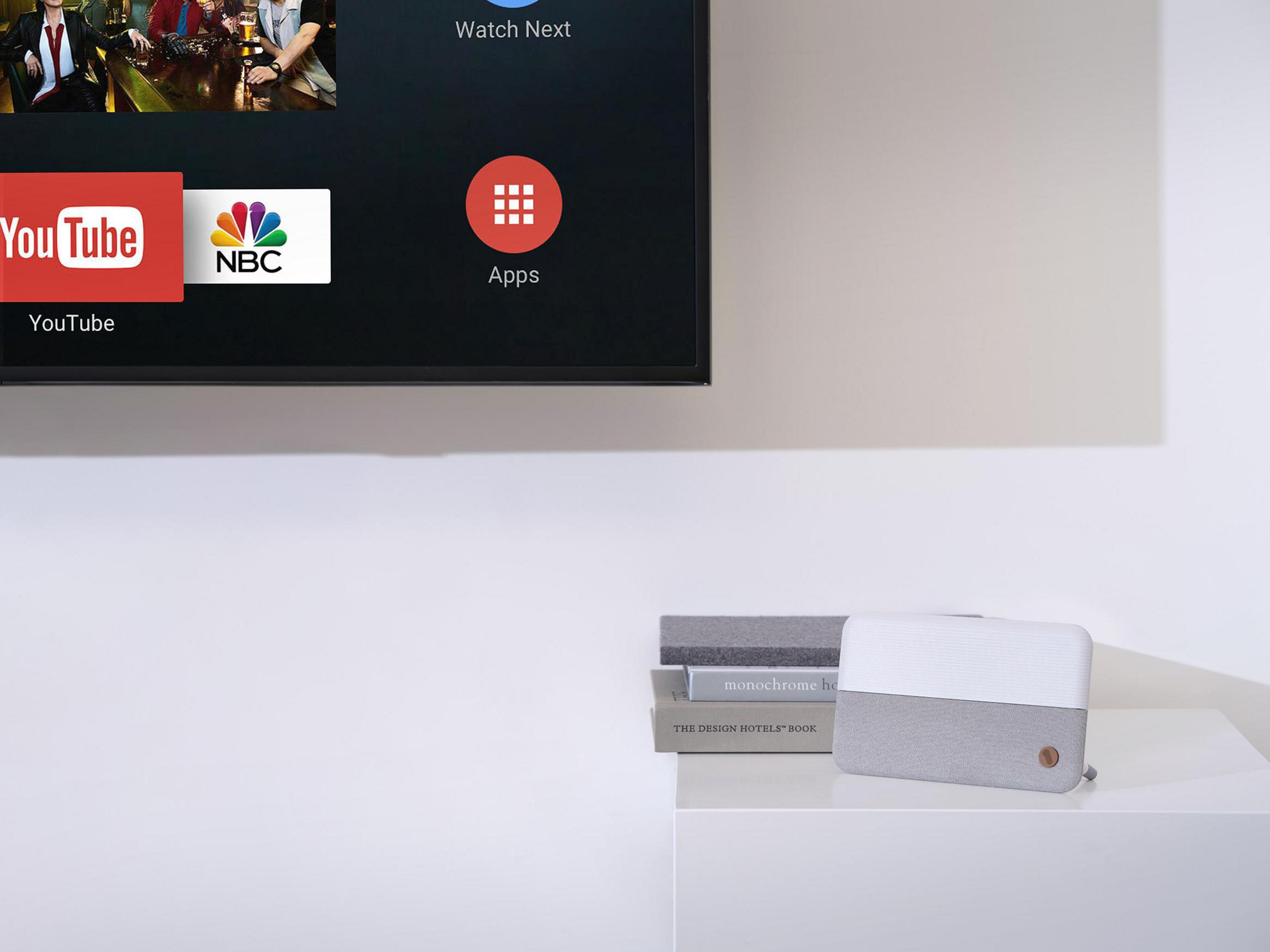 Ekran telewizora z aplikacjami YouTube i NBC. Biała półka z głośnikiem.