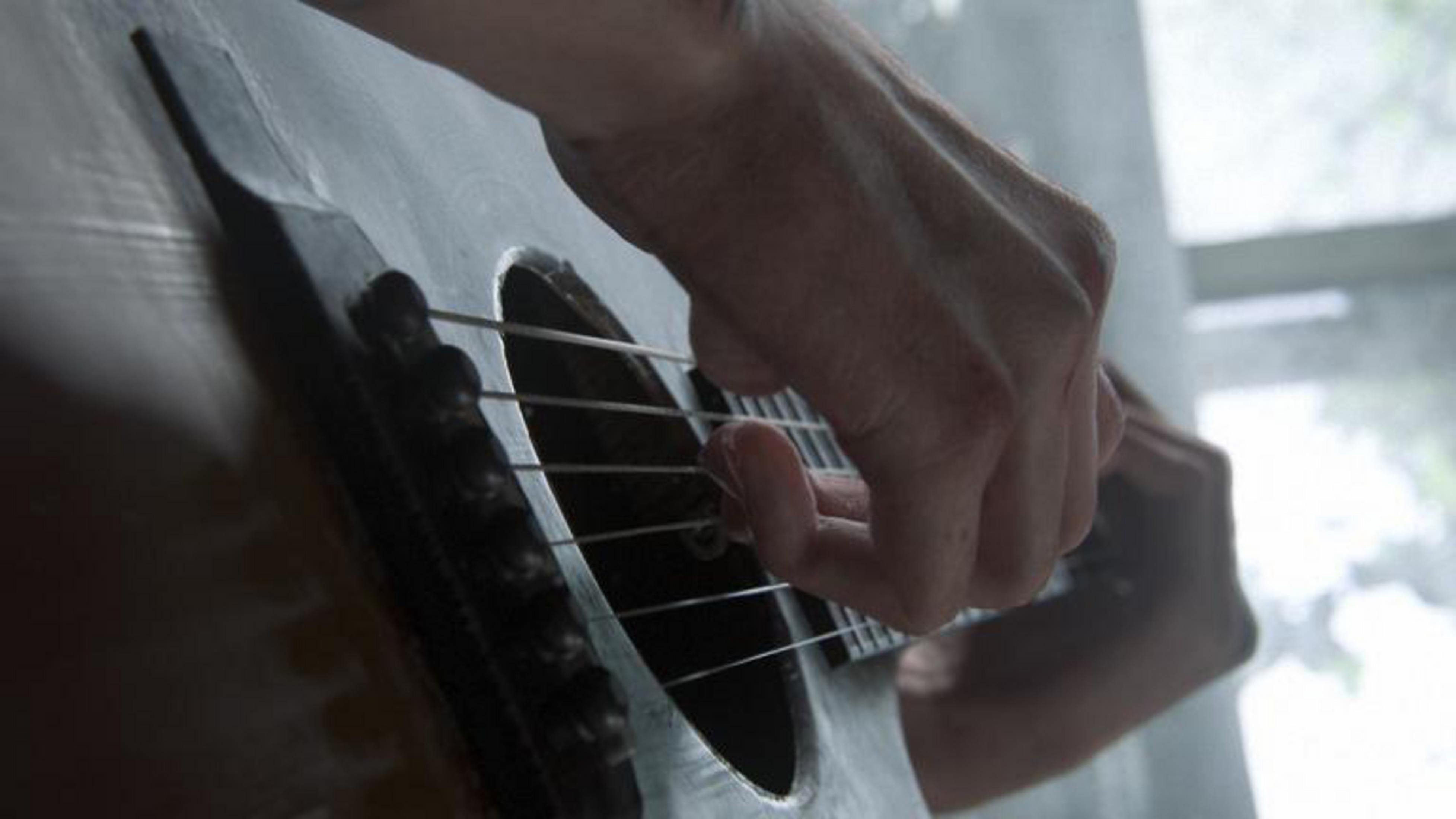 Primo piano di mani che suonano la chitarra, con focus sulle corde e le dita.