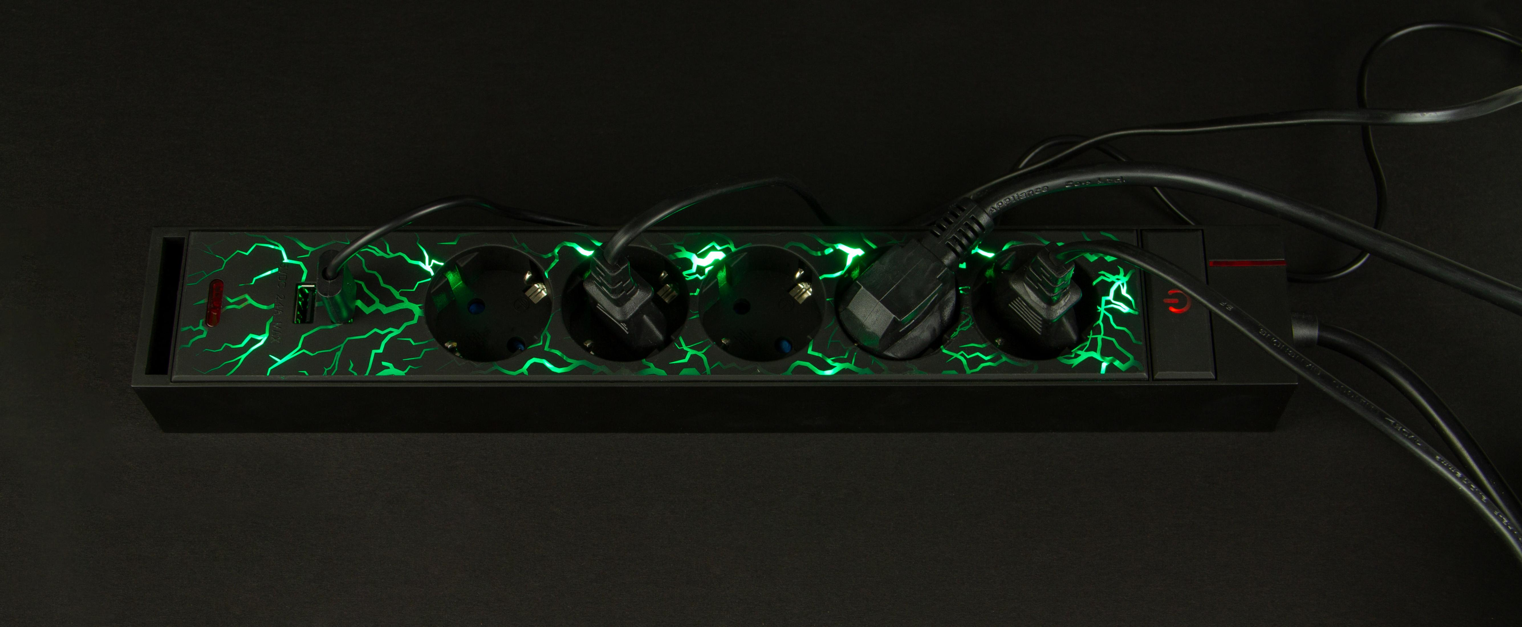 Schwarze Steckdosenleiste mit grünem Blitzeffekt. Kabel angeschlossen, schwarzer Hintergrund.