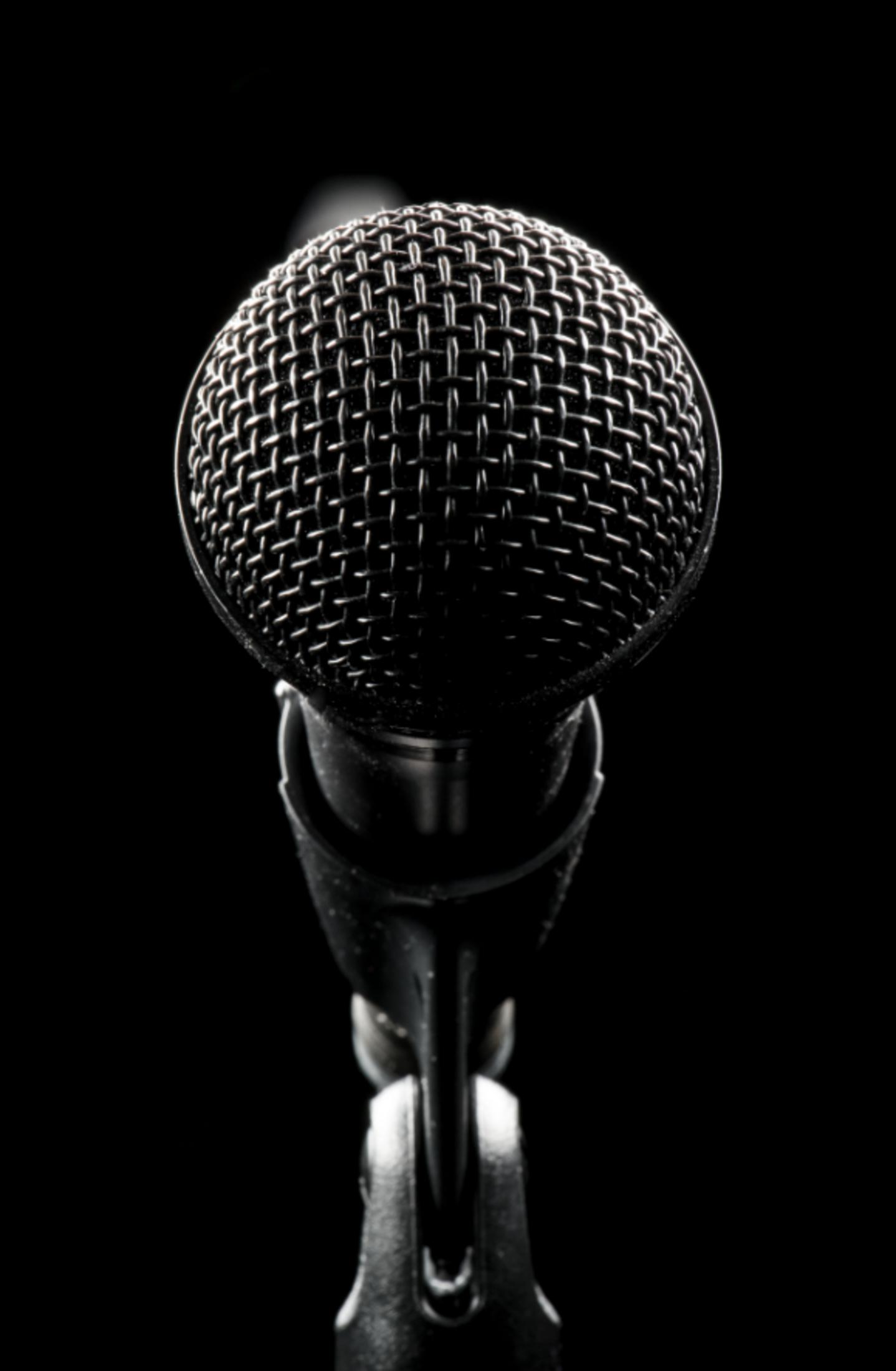 Zbliżenie czarnego mikrofonu na statywie na czarnym tle.