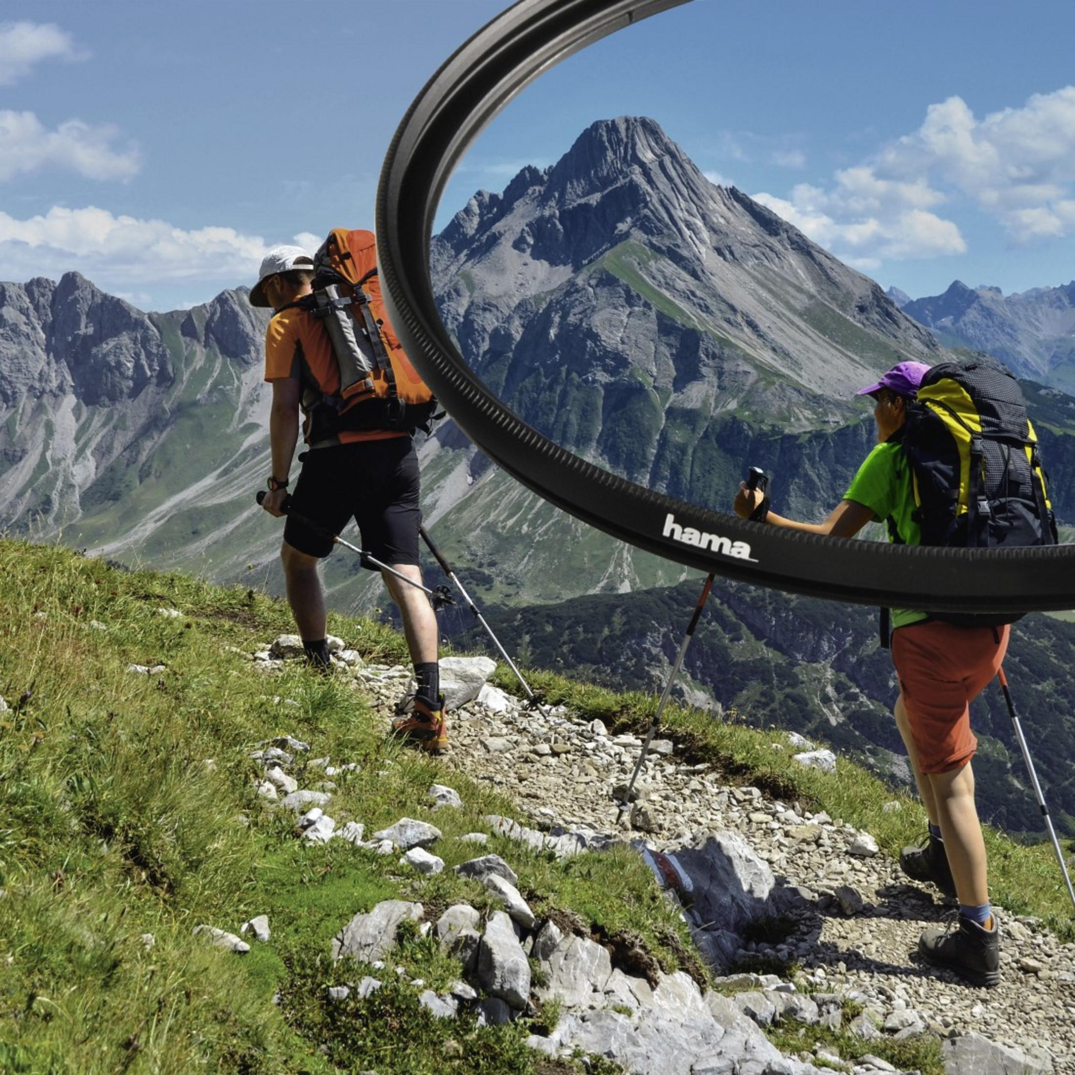 Turyści na górskim szlaku. Logo Hama w zakrzywionej ramie. Widok na góry w tle. Błękitne niebo.