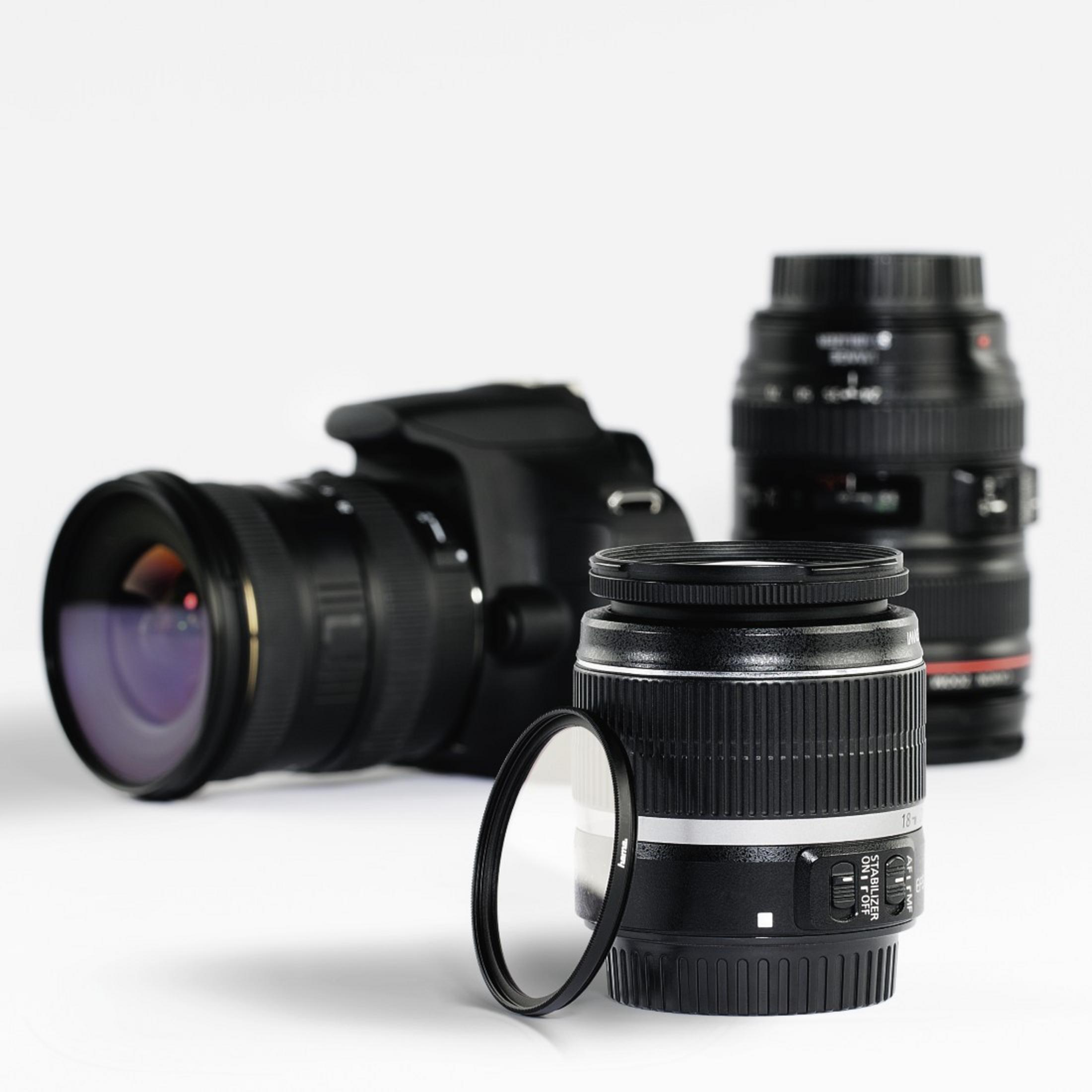 Obiektywy i korpus aparatu na białej powierzchni. Jeden obiektyw ma filtr.