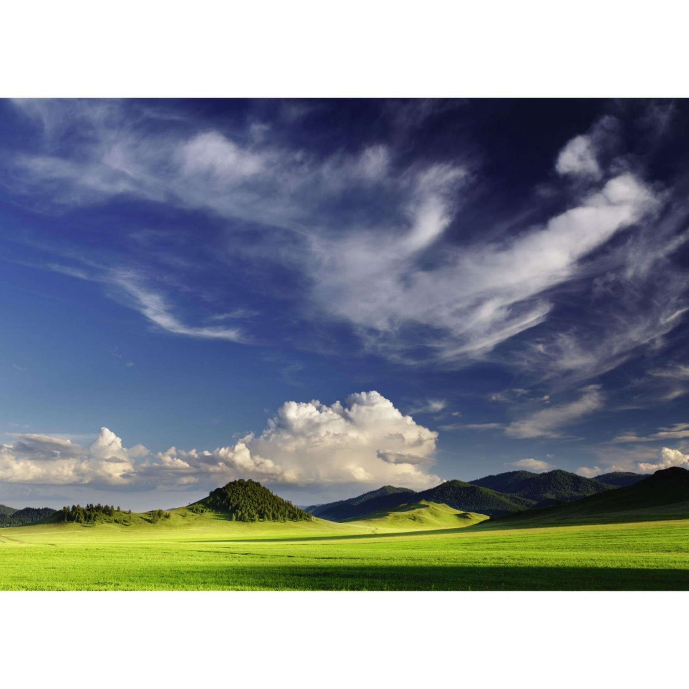 Weite Landschaft mit grünem Feld, Hügeln und blauem Himmel mit Wolken.