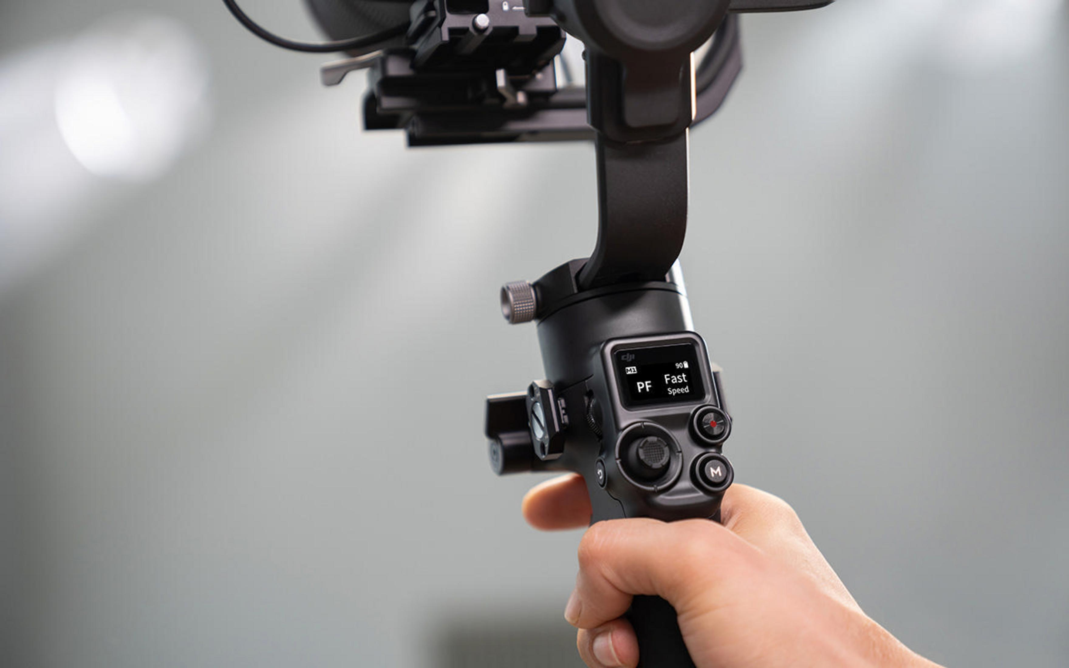 Eine Person hält einen schwarzen Gimbal-Stabilisator. Der Controller zeigt 'PF' und 'Fast Speed'.