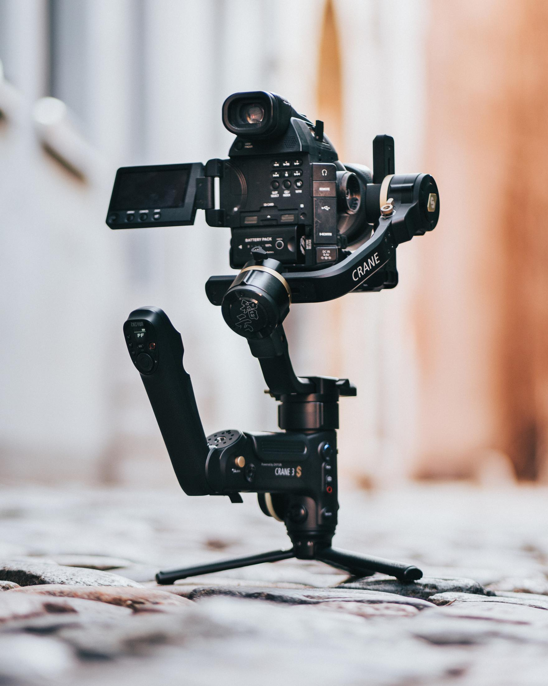 Una telecamera nera su un treppiede nero, posizionata su una pavimentazione. La telecamera è un'impostazione di ripresa.