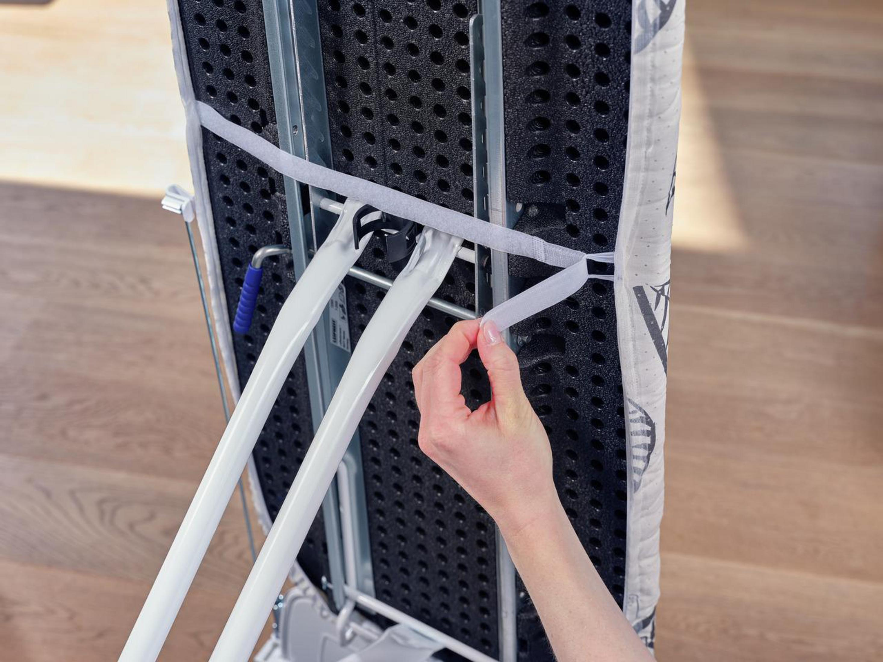 Ręka zapina pasek na rzep na spodzie deski do prasowania.