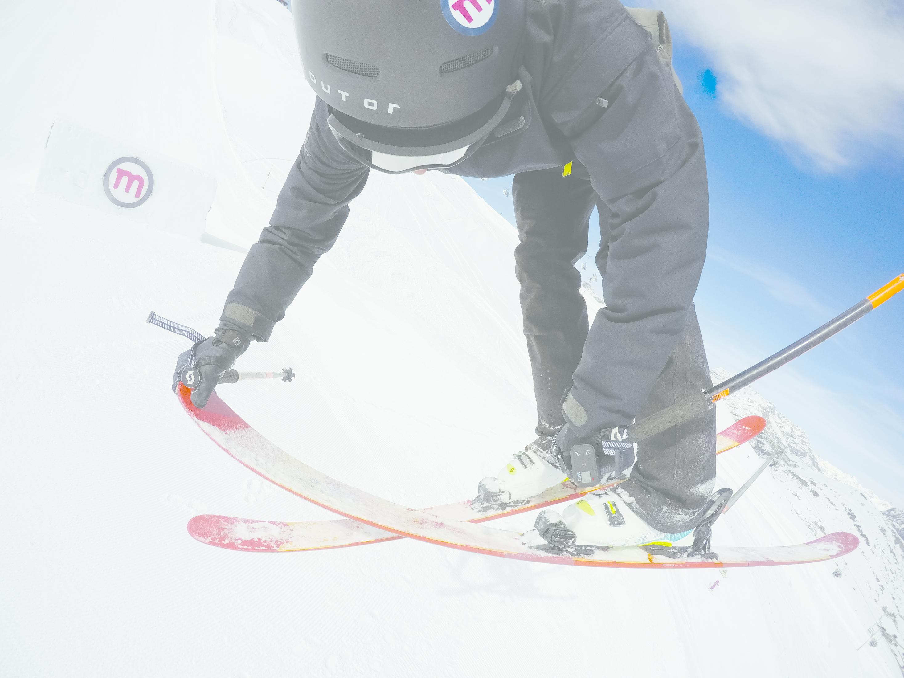 Sciare sugli sci, ripresa dal basso, montagna innevata. La persona è piegata.